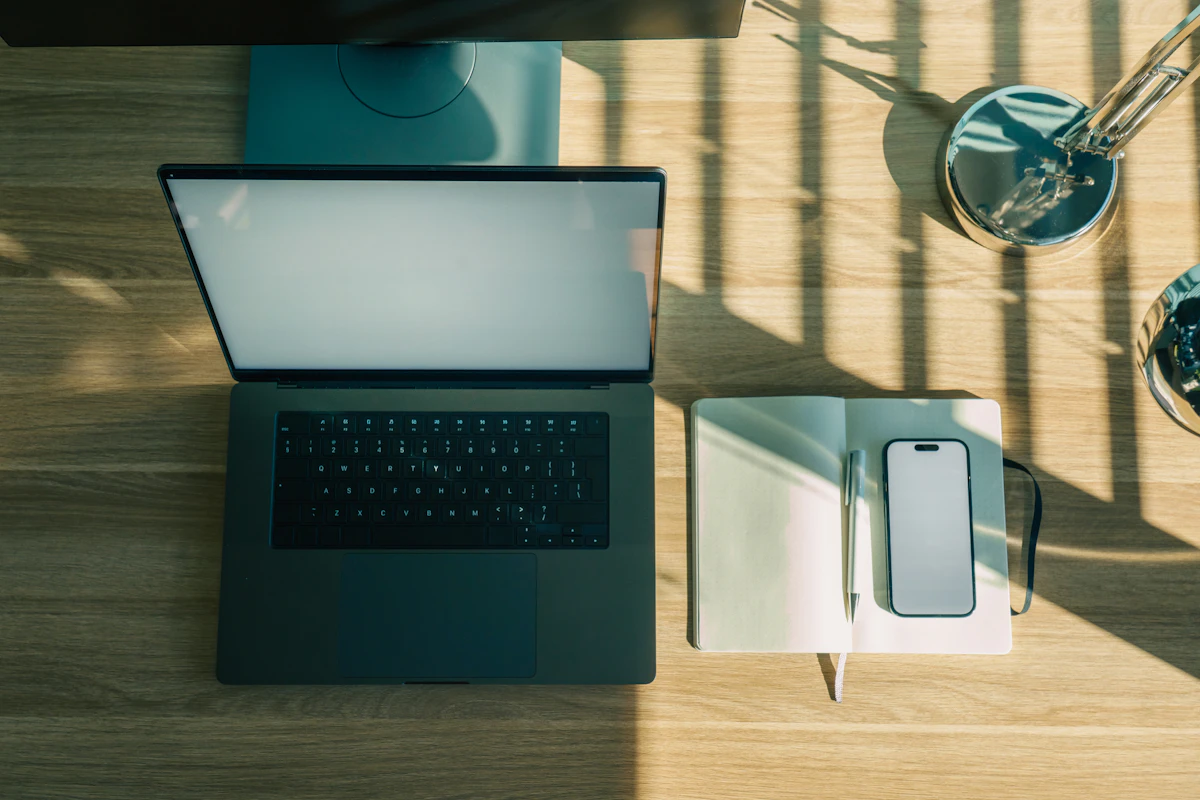 Laptop, phone, and notebook on a wooden desk.