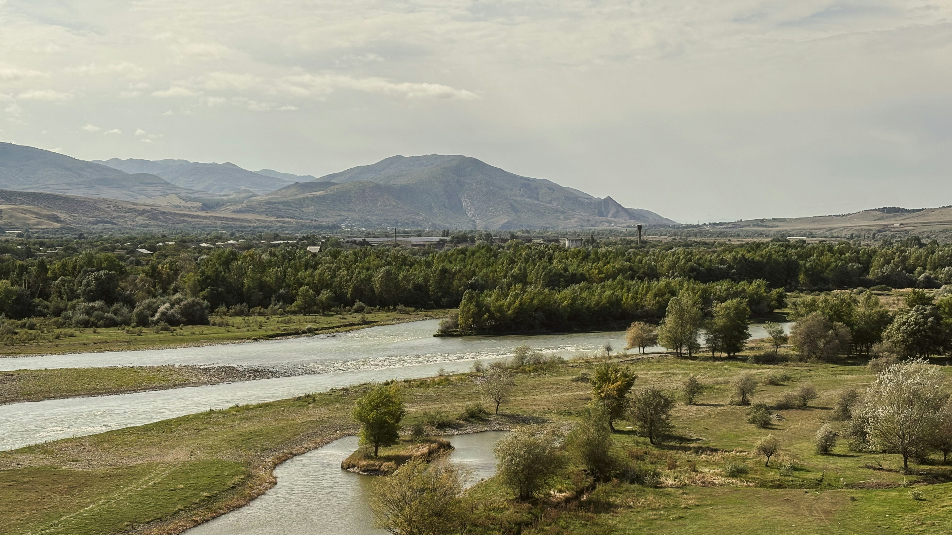 A wide river flows through a green landscape with mountains.