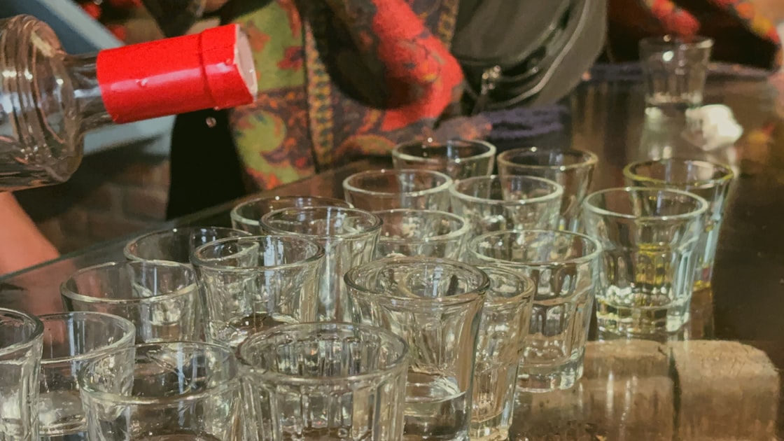 Pouring liquor into many small shot glasses.