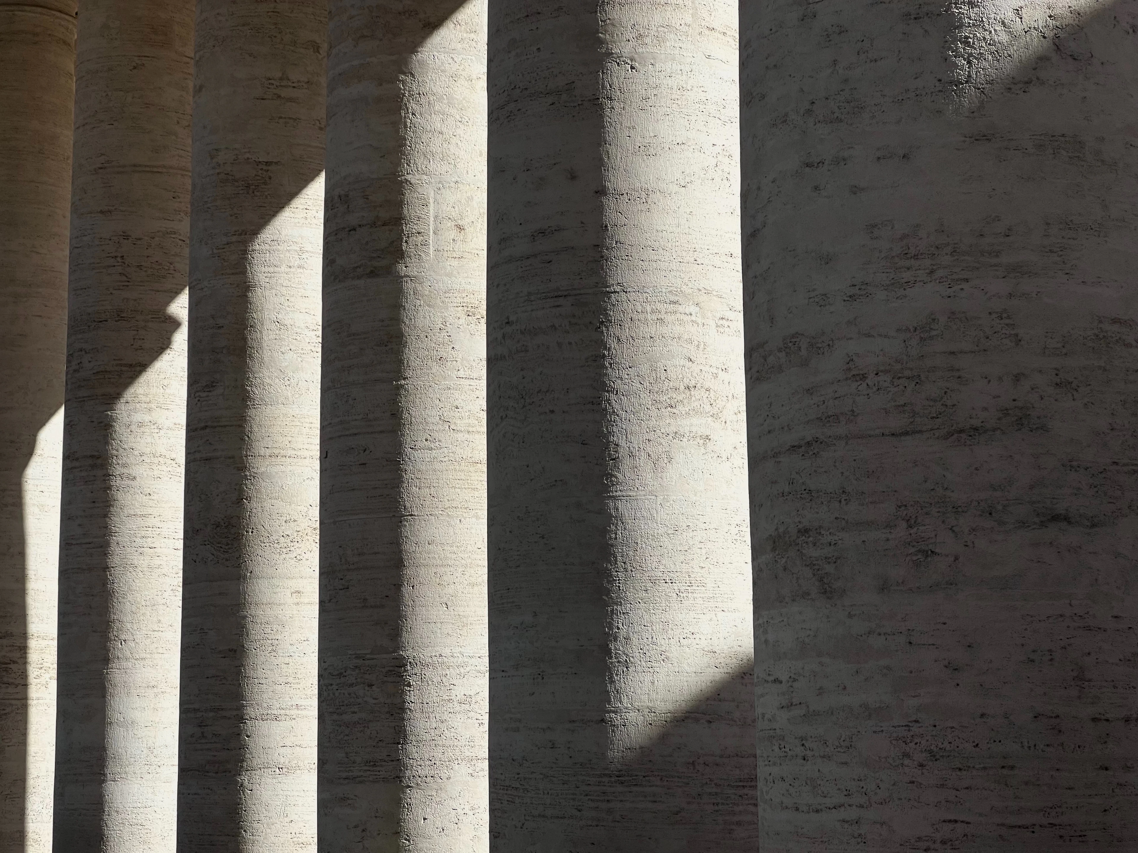 Row of pale stone columns casting strong, rhythmic shadows