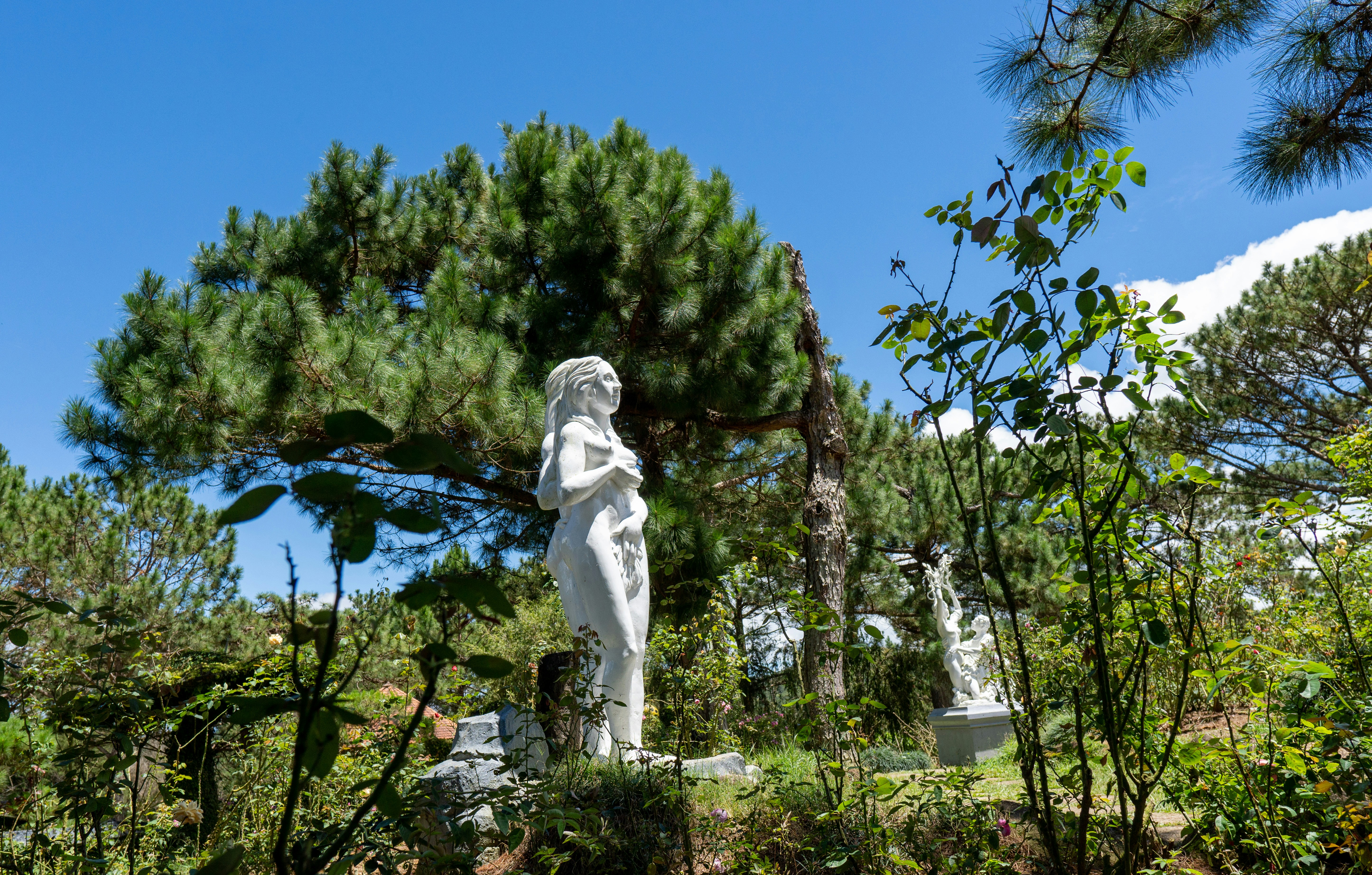 White statue in a lush green garden under blue sky.