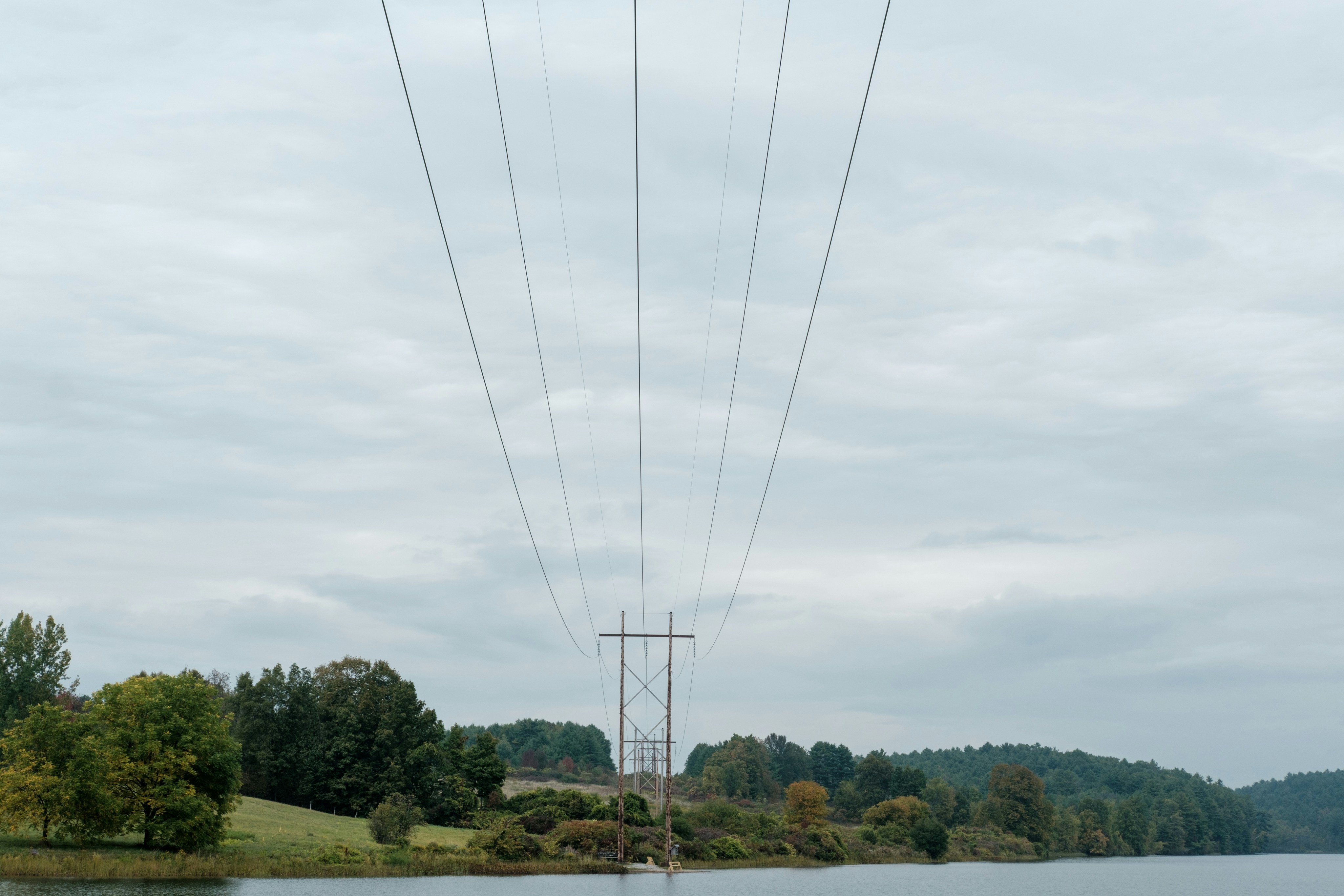 Power lines cross a calm lake under cloudy skies.