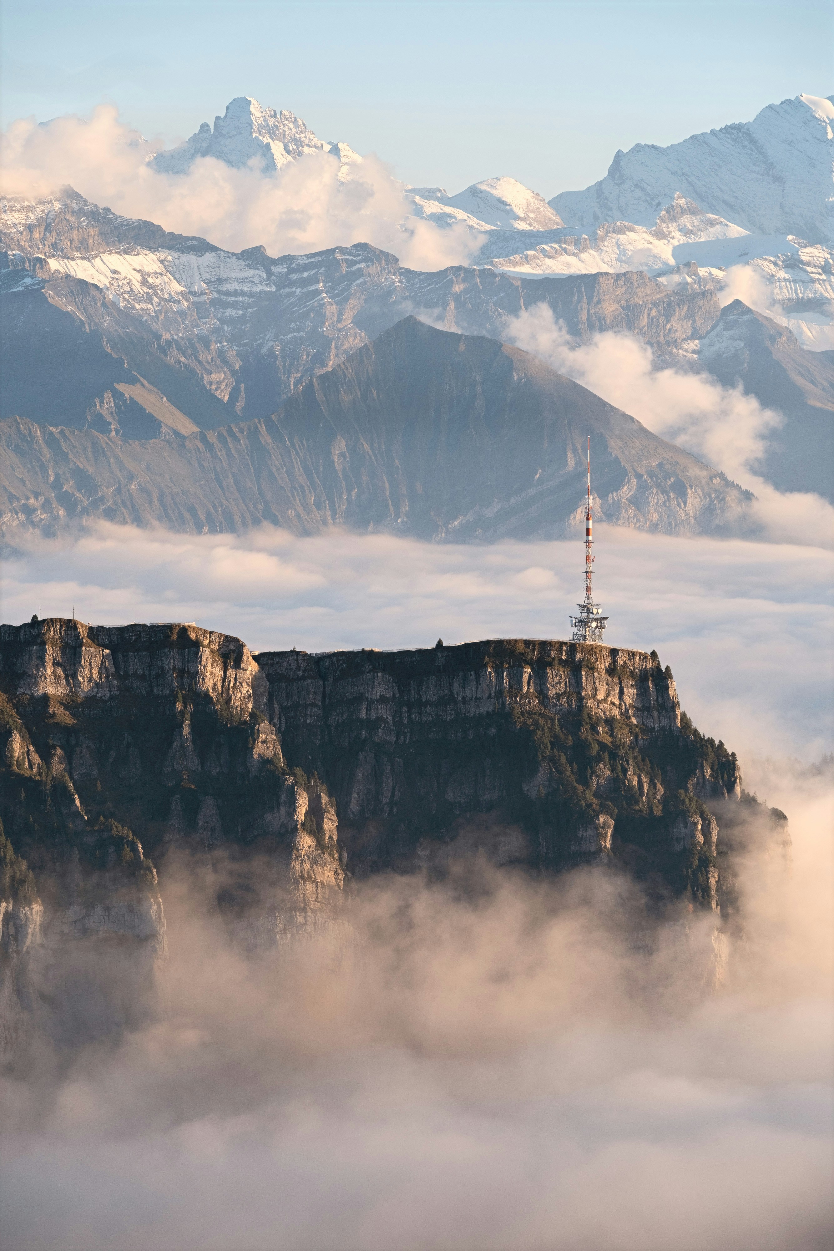 Tower on a cliff above clouds with snowy mountains.