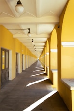 Long yellow hallway with arched openings and sunlight patterns.