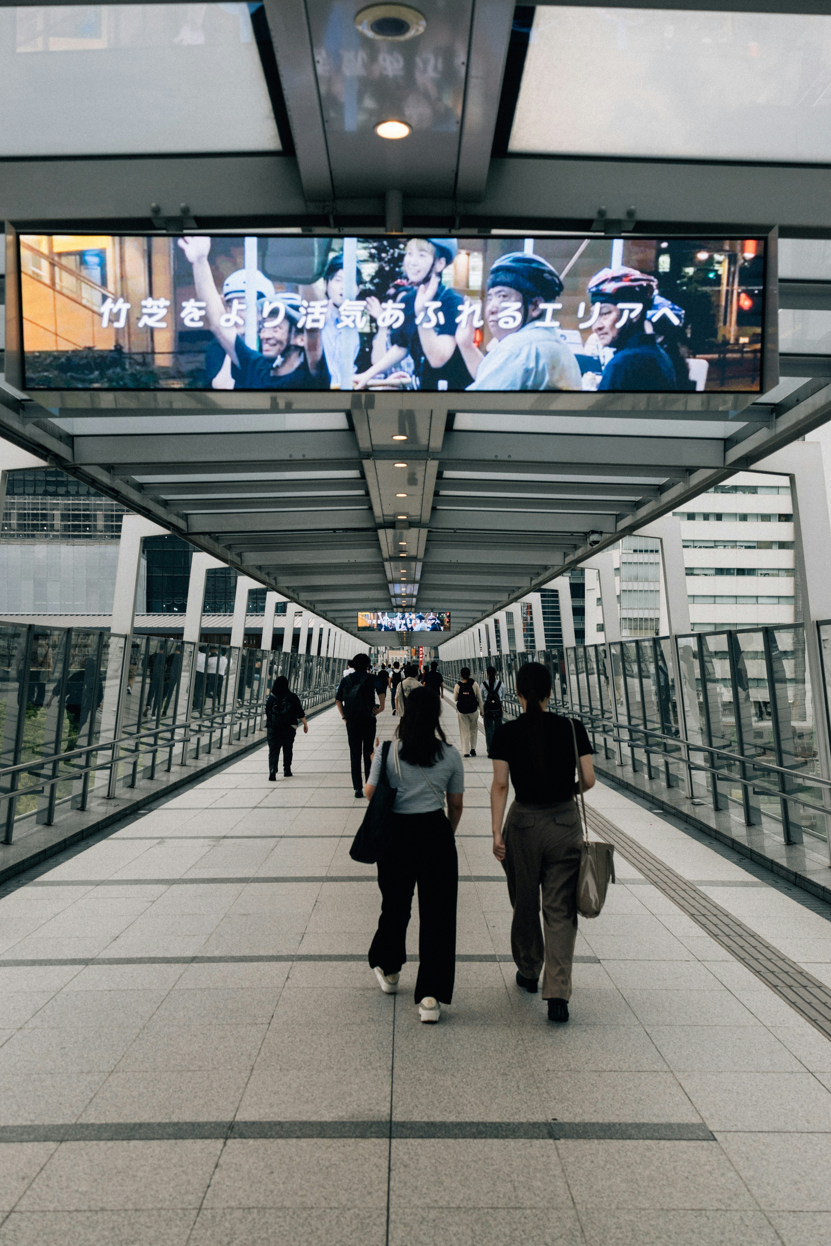 People walking on a modern elevated walkway with advertisements.