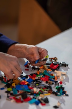 Hands building with colorful toy blocks on white surface.