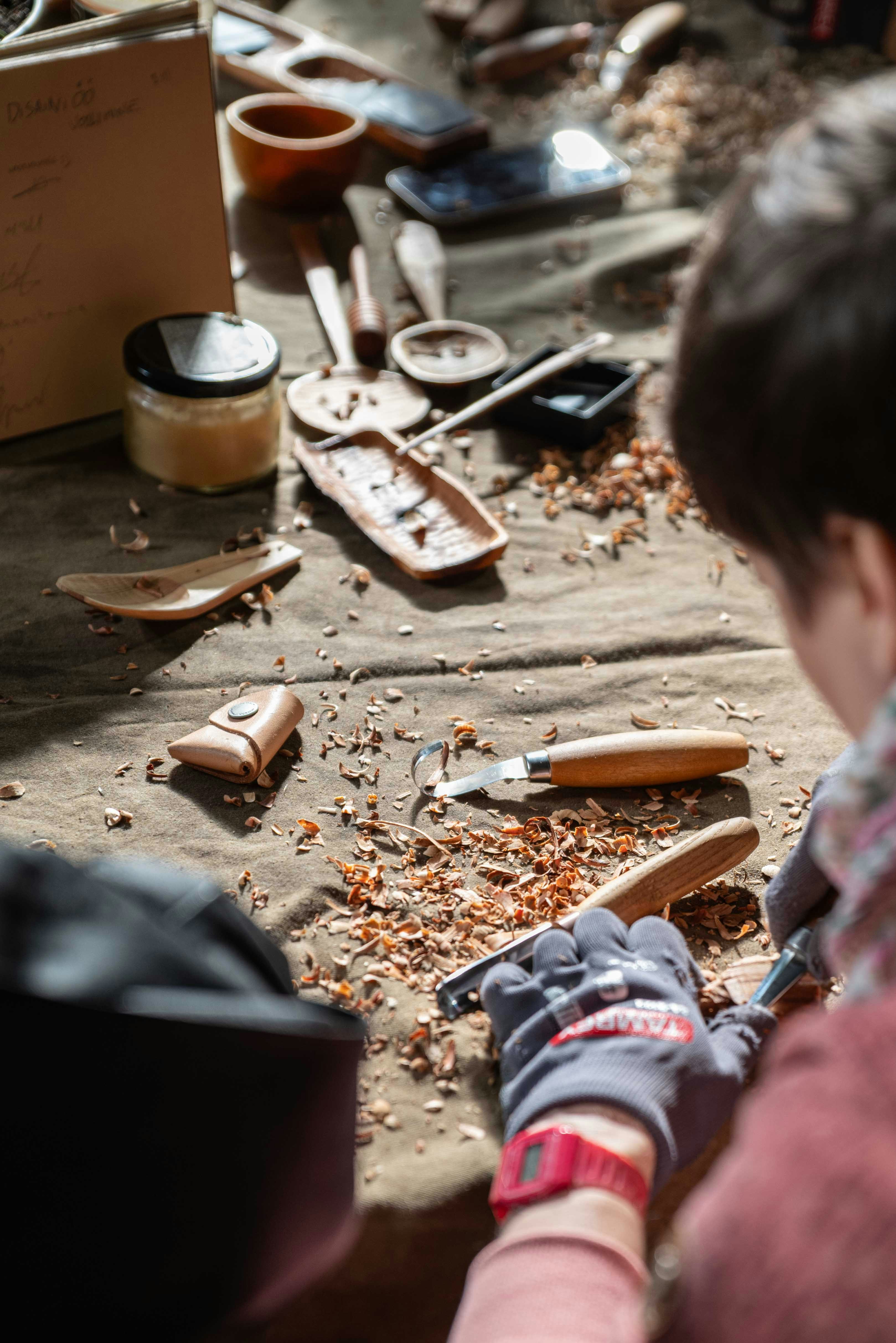 Person carving wood with tools and shavings