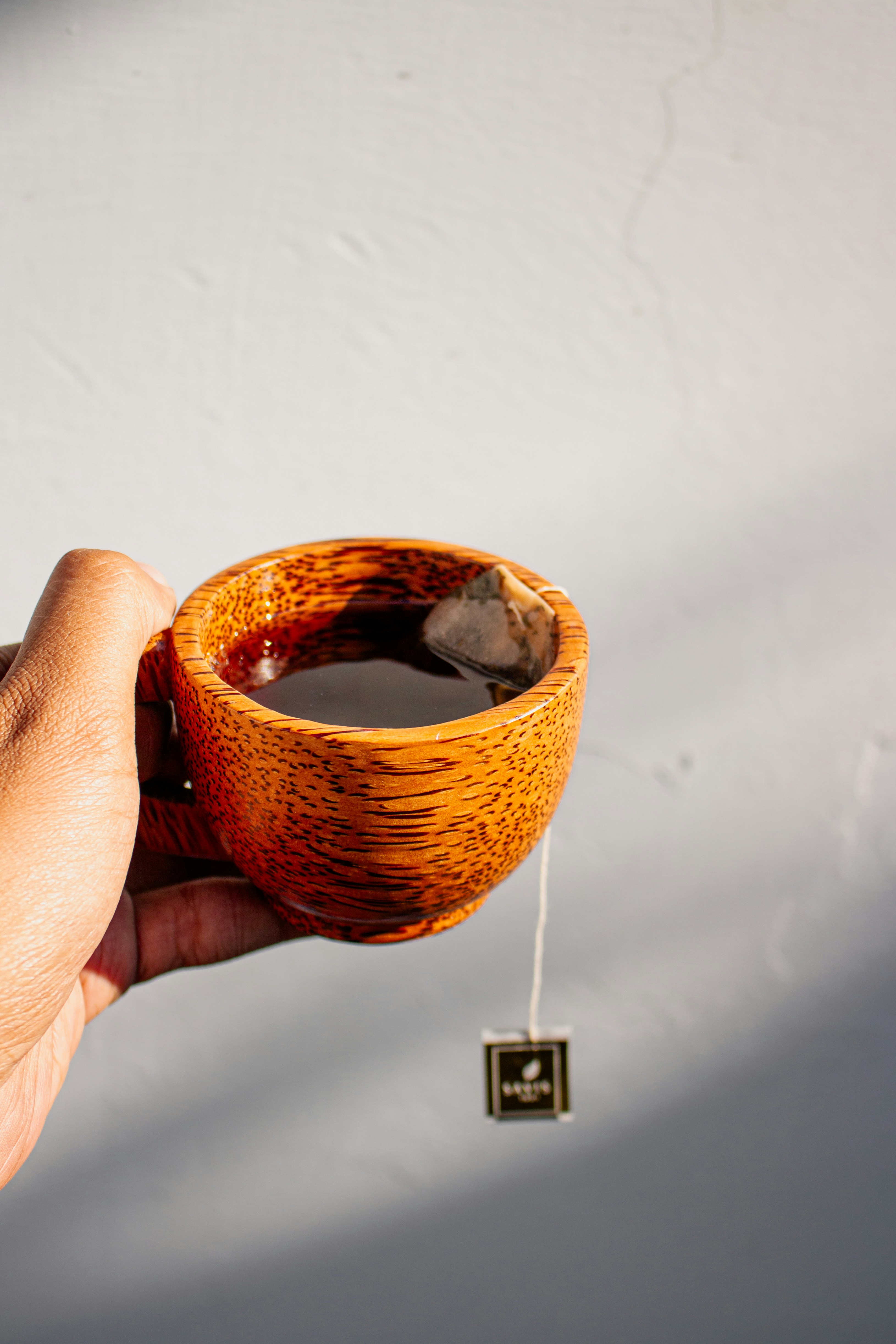 Hand mit einer hölzernen Tasse Tee mit Teebeutel.