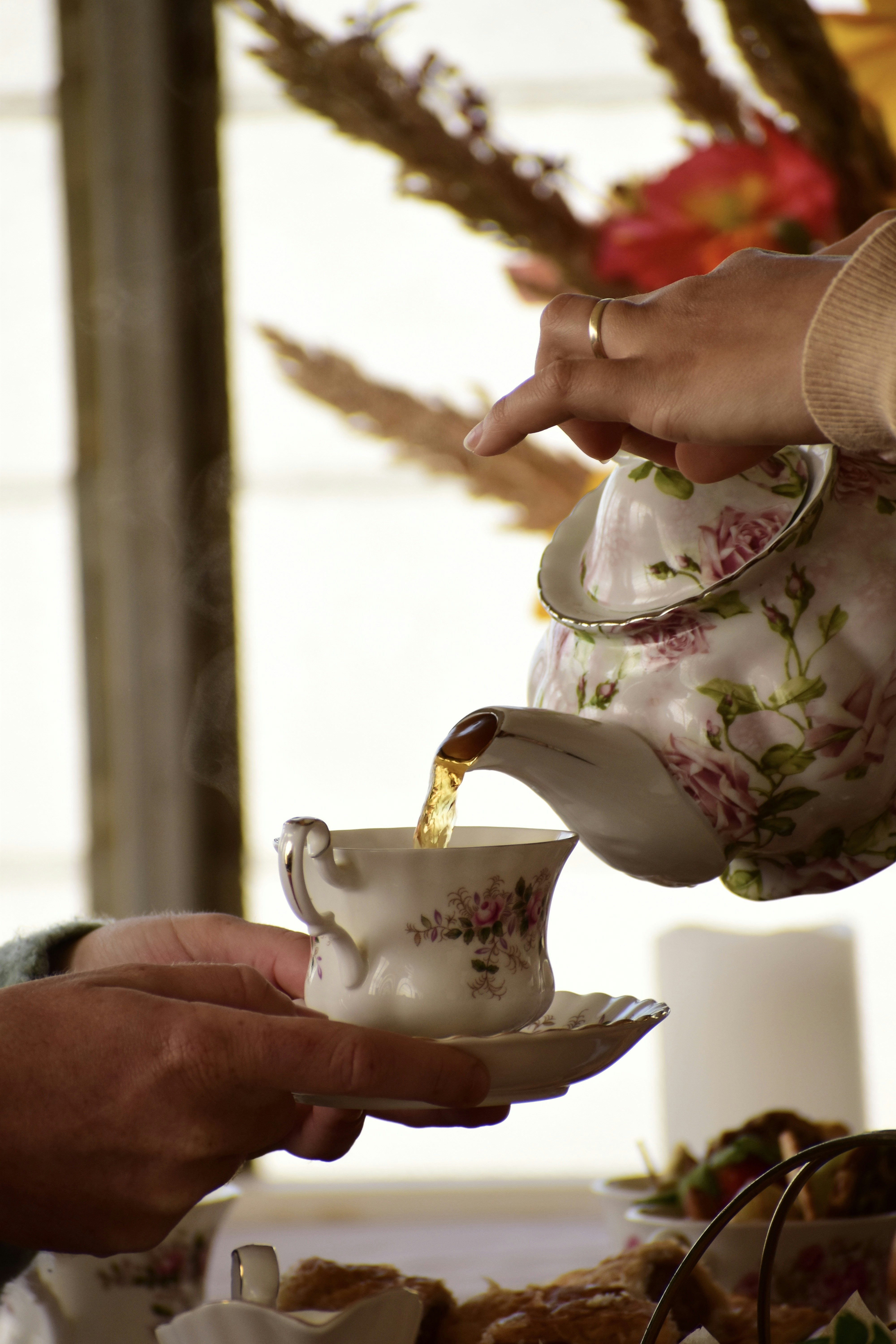 Tea is poured from a floral teapot into a cup.
