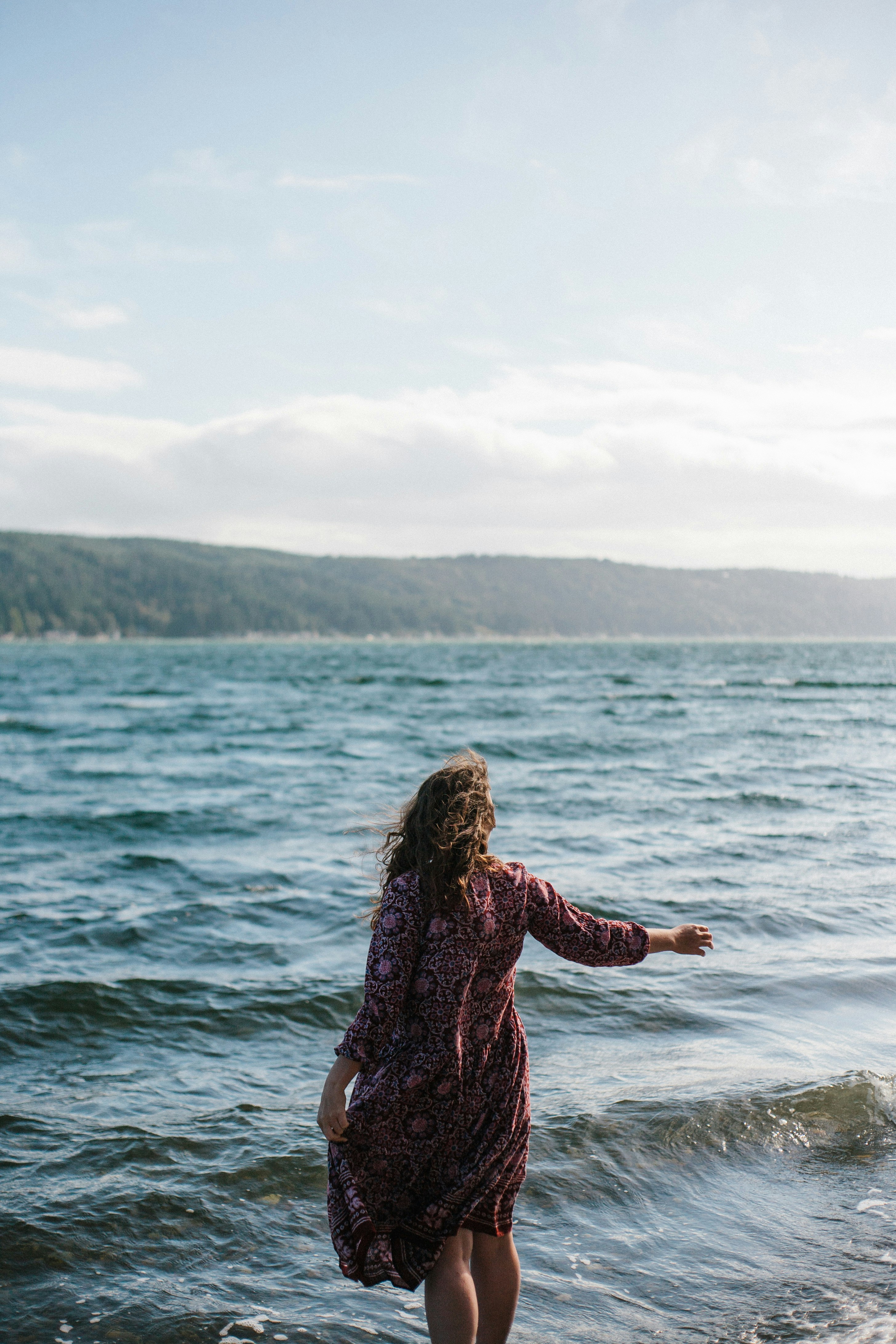 Une femme en robe se tient près des vagues de l’océan.