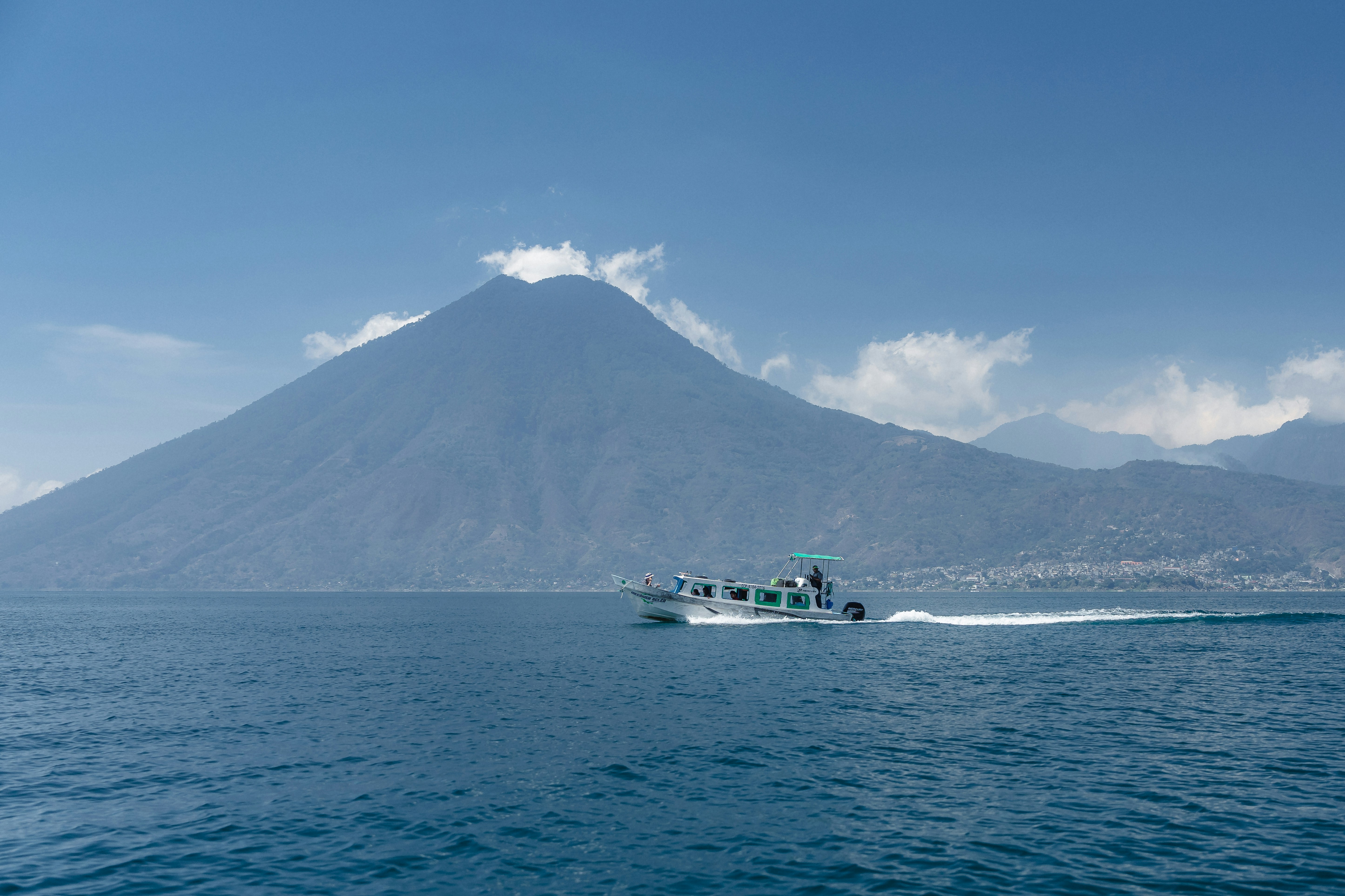 Un bateau navigue paisiblement sur le lac Atitlan avec un volcan majestueux se dressant en arrière-plan sous le soleil.