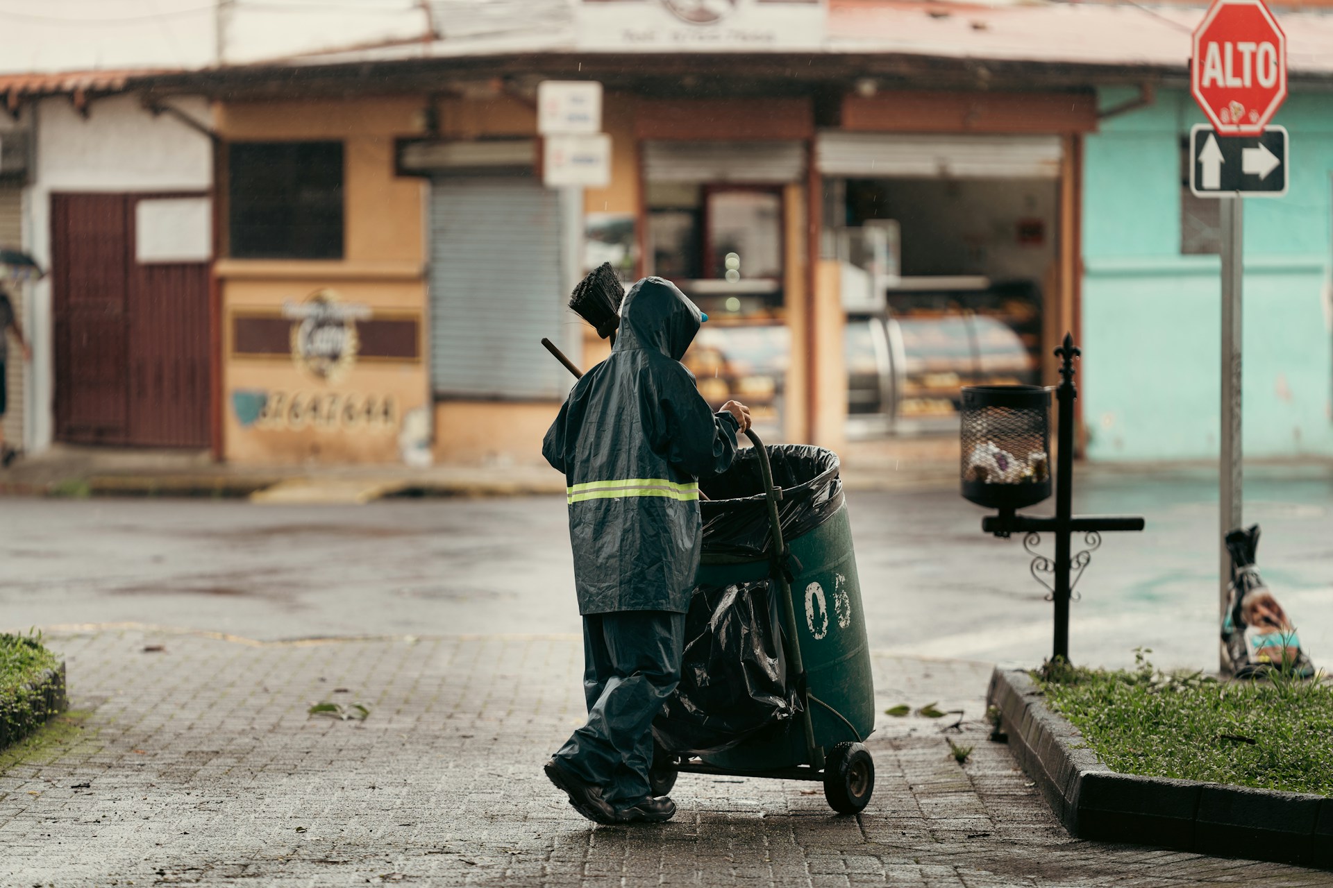 Sanitation worker pushing trash cart on wet street.