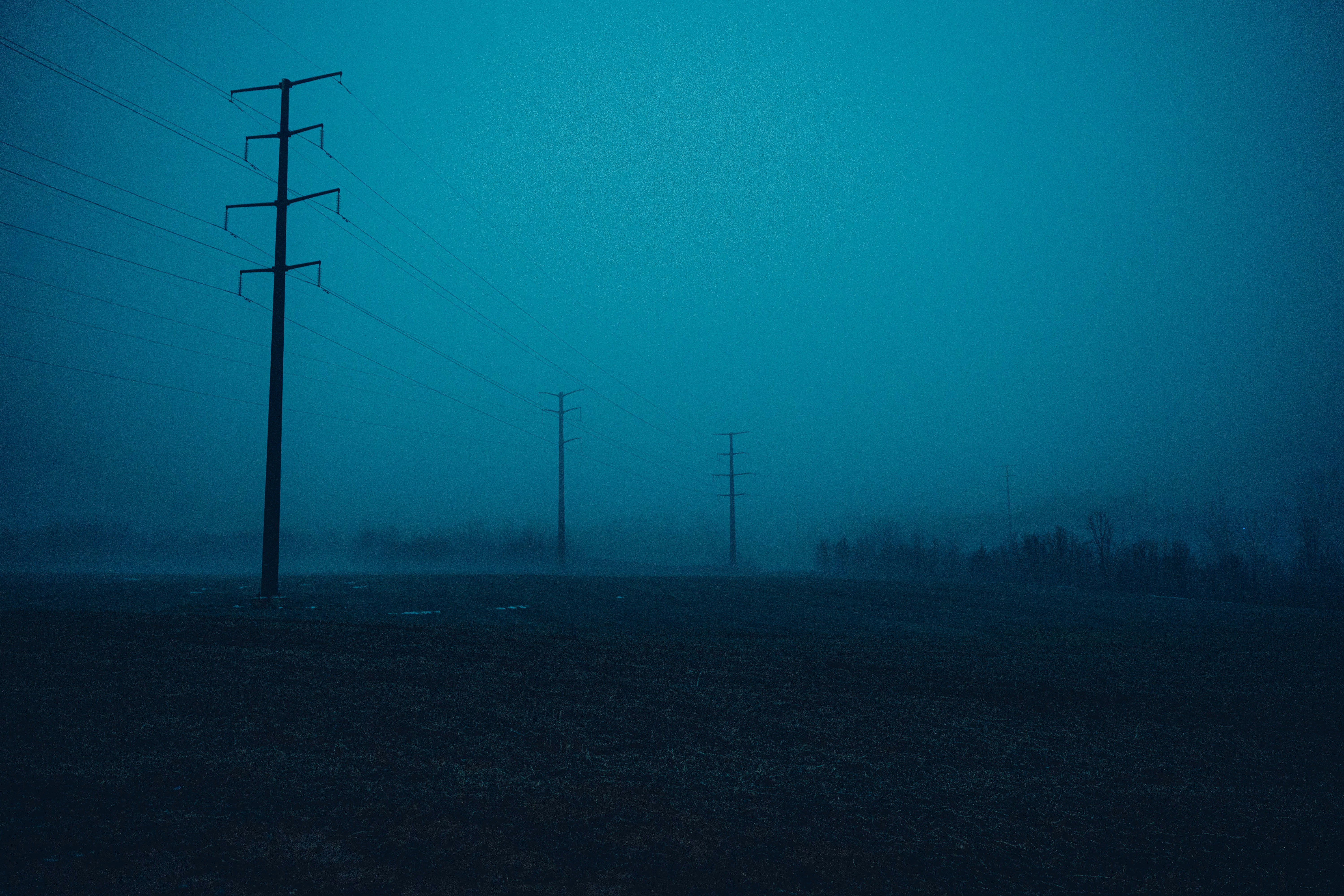 Power lines in a foggy, dark landscape at dusk.