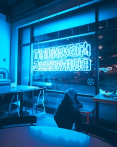 Person sitting in dimly lit cafe with neon sign.