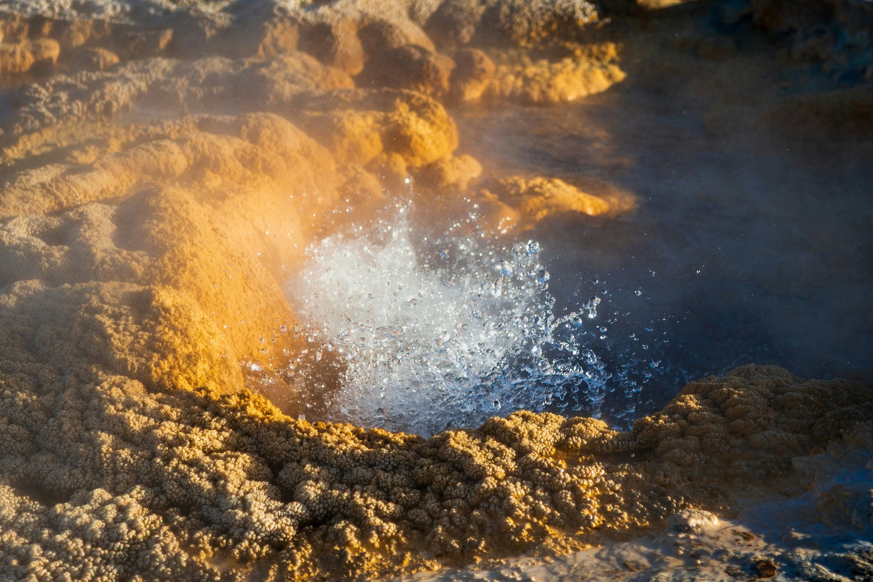 Hot spring erupting with steam and mineral deposits.