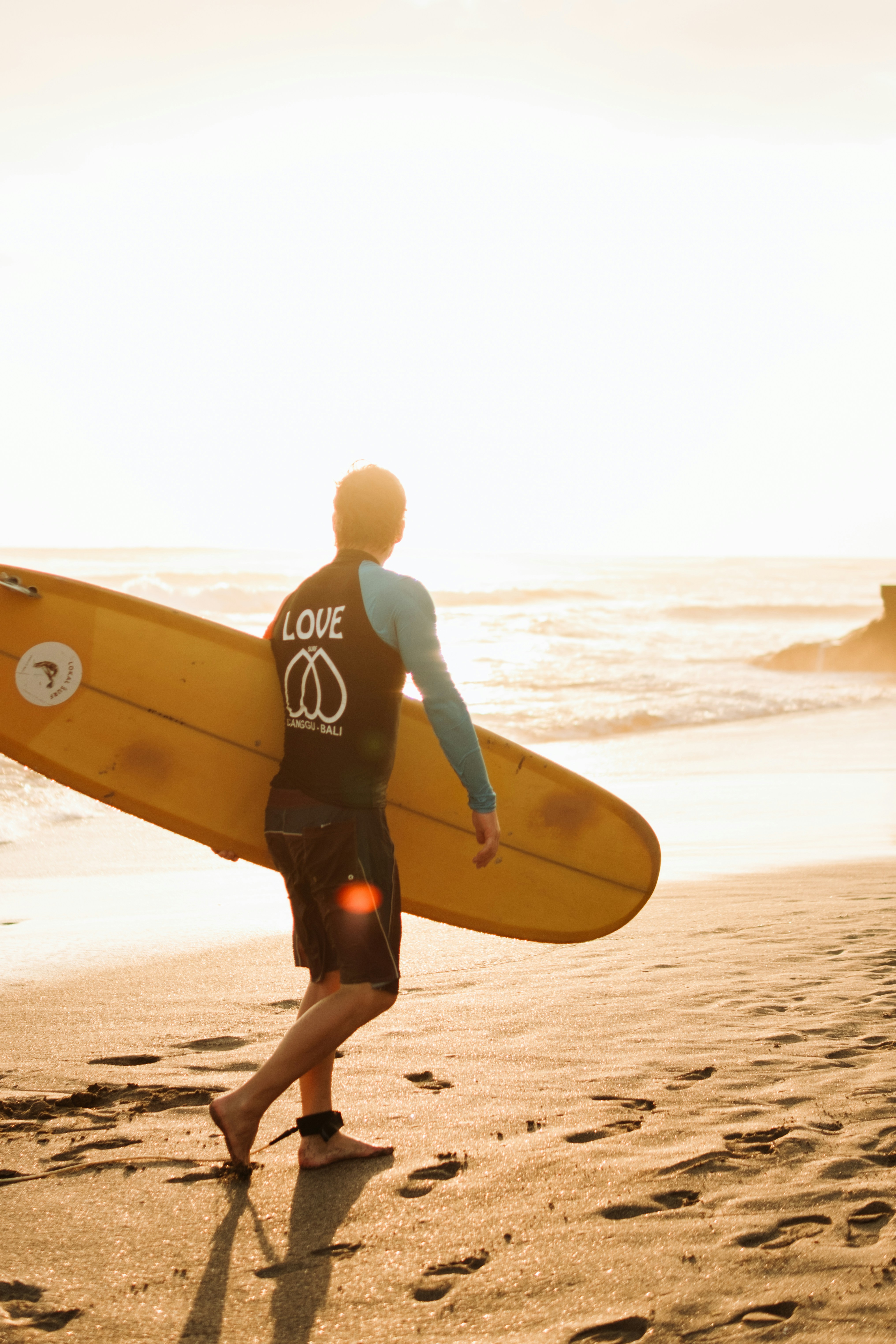 Surfer walking on beach with surfboard at sunset