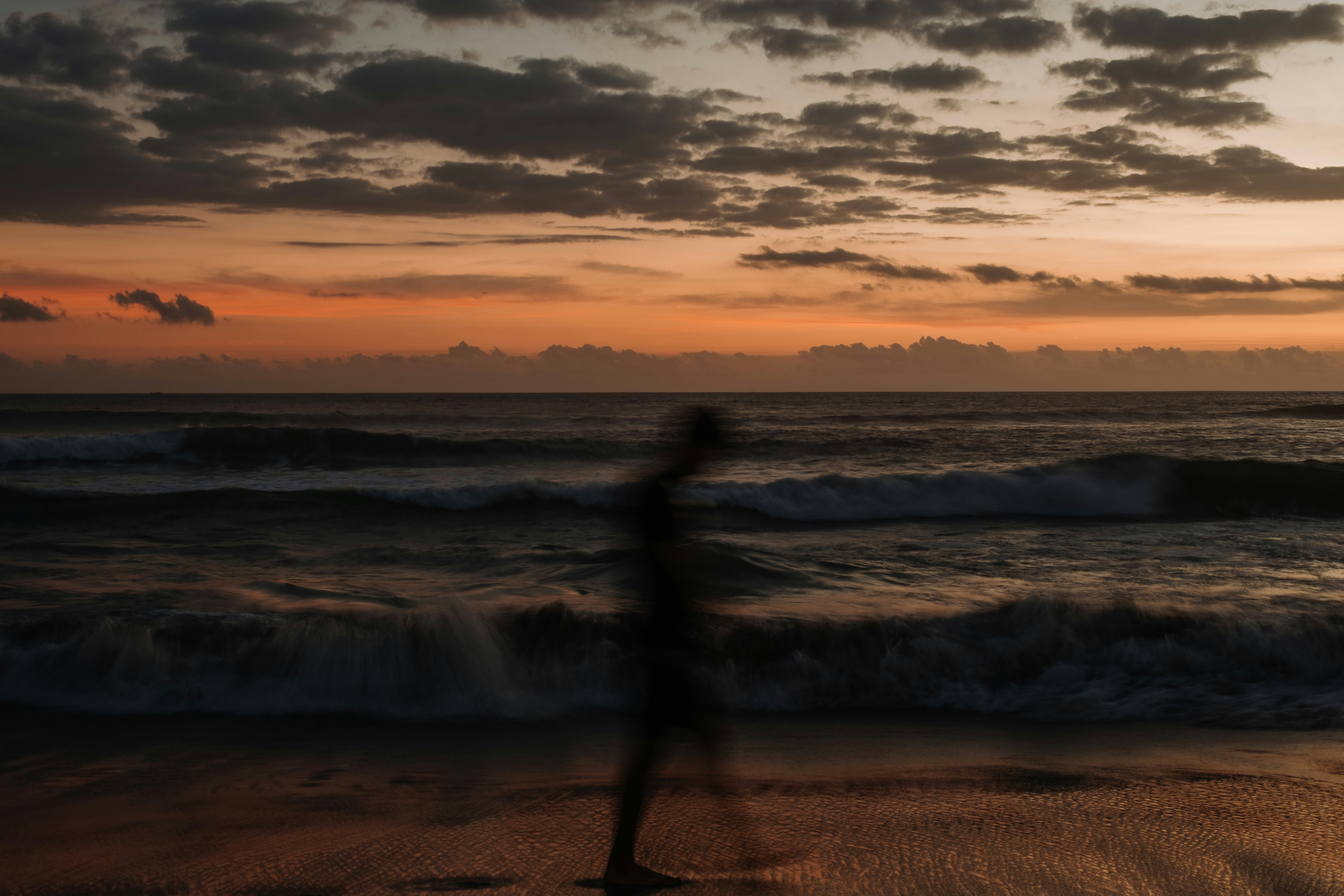 A blurred figure walks on a beach at sunset