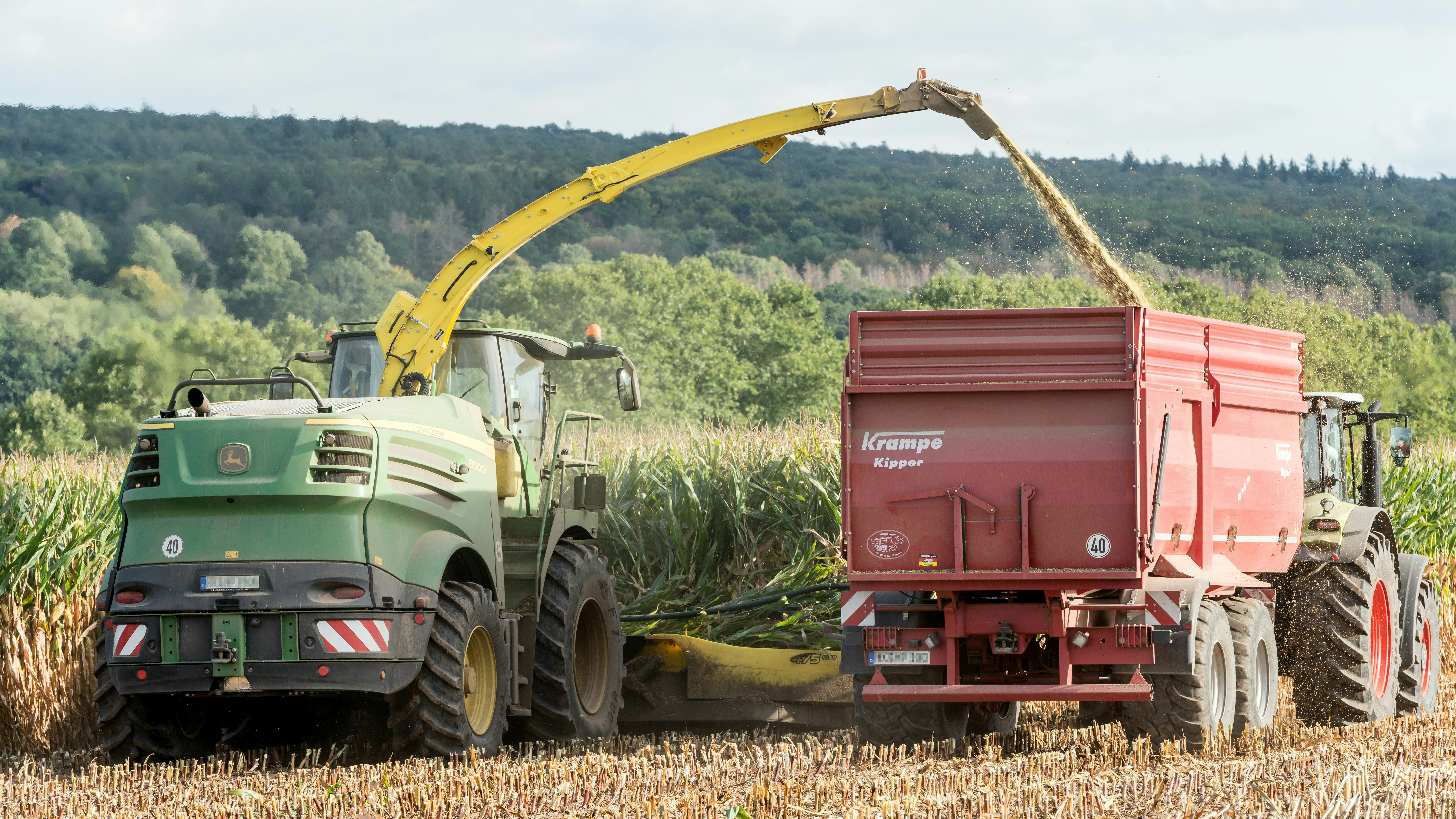 Green harvester loading chopped corn into red trailer