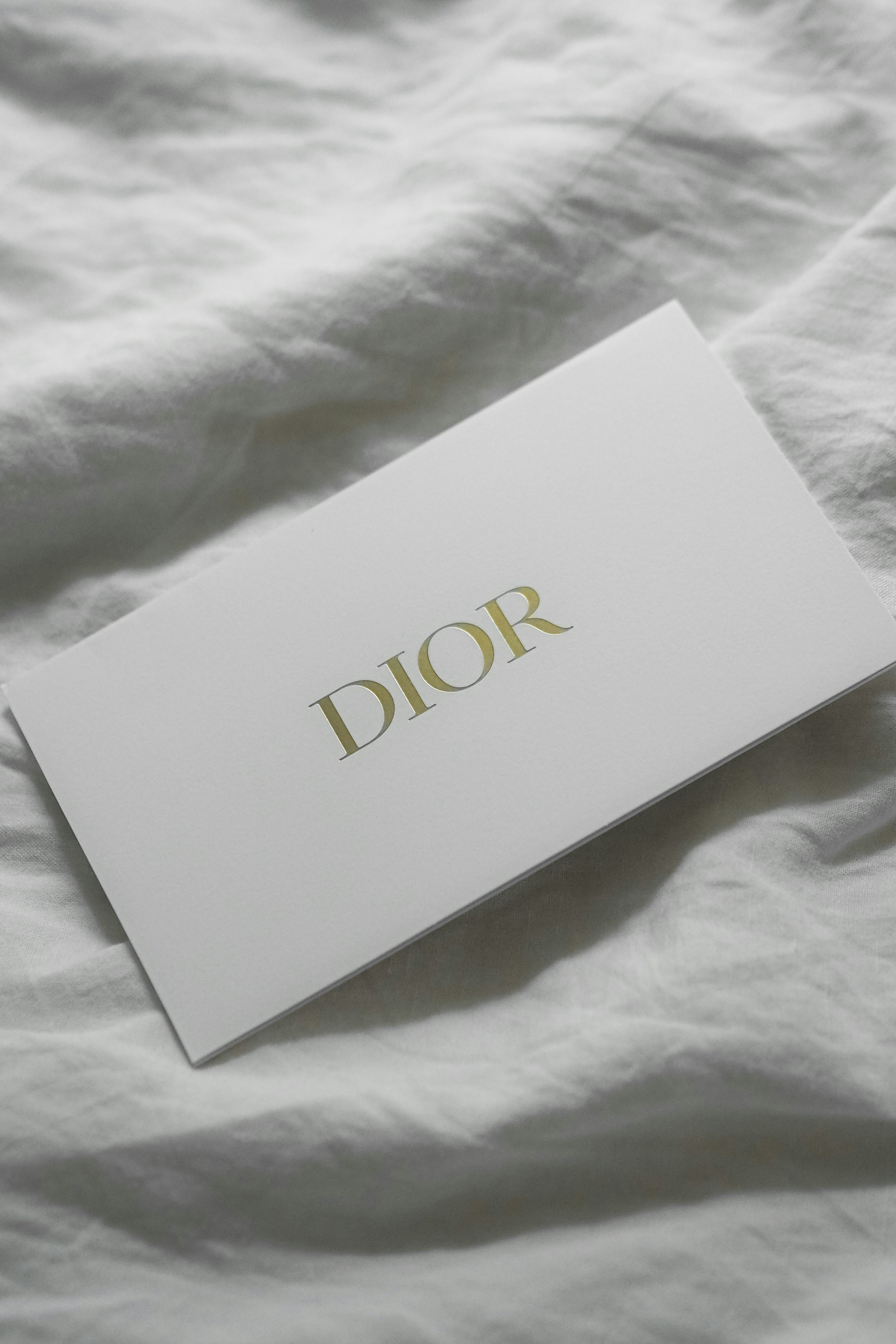 White dior card on a wrinkled white sheet