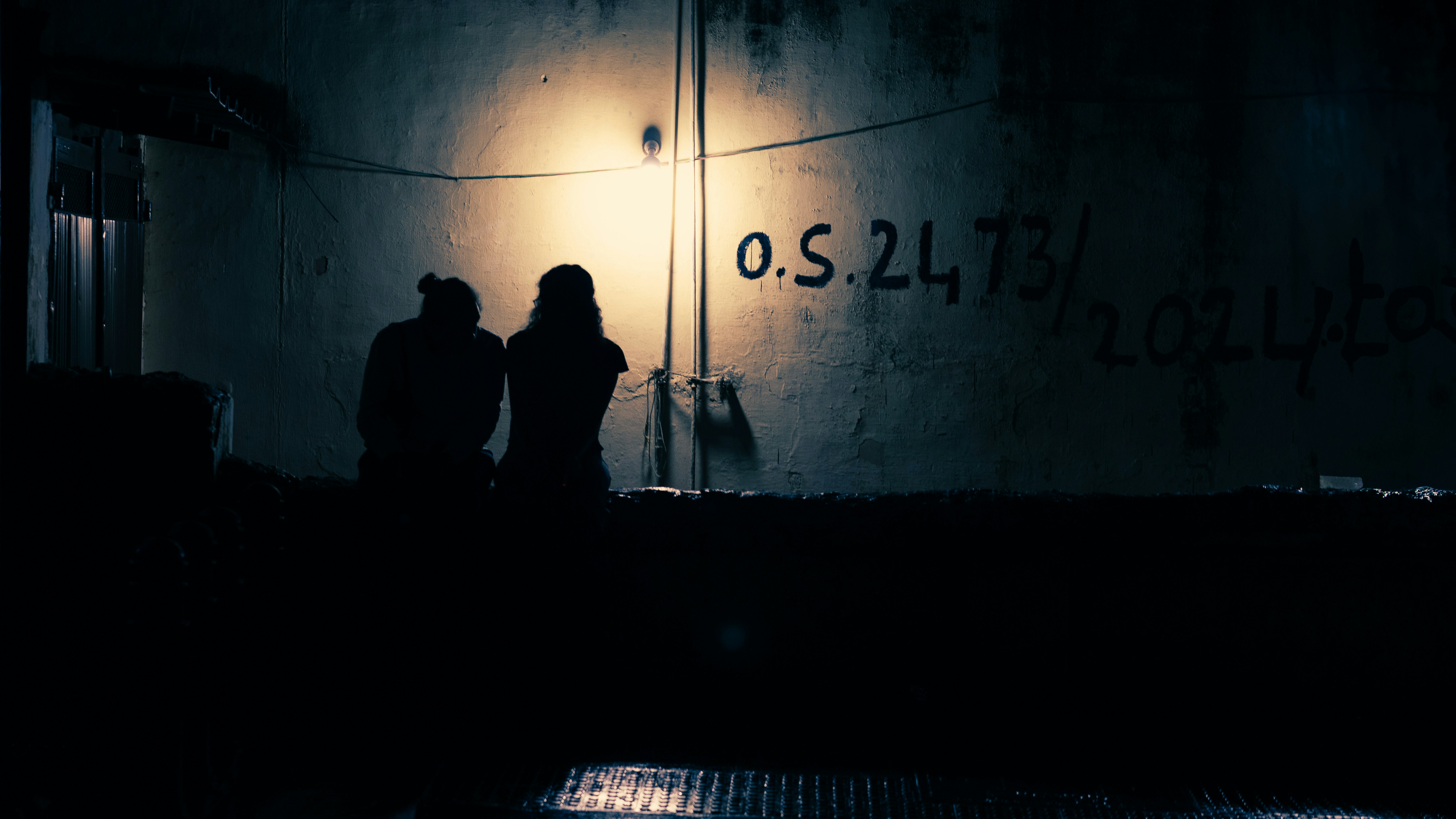 Two figures silhouetted against a lit wall at night.