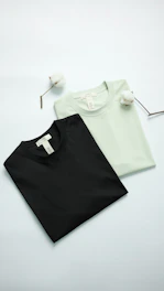 Two t-shirts, black and light green, with cotton sprigs.