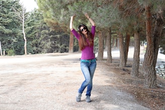 Woman in purple shirt and jeans dancing outdoors.