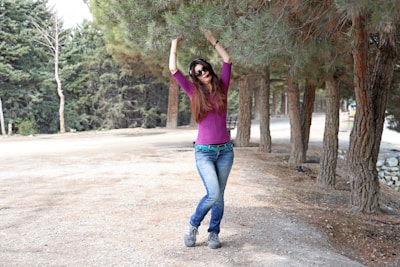 Woman in purple shirt and jeans dancing outdoors.