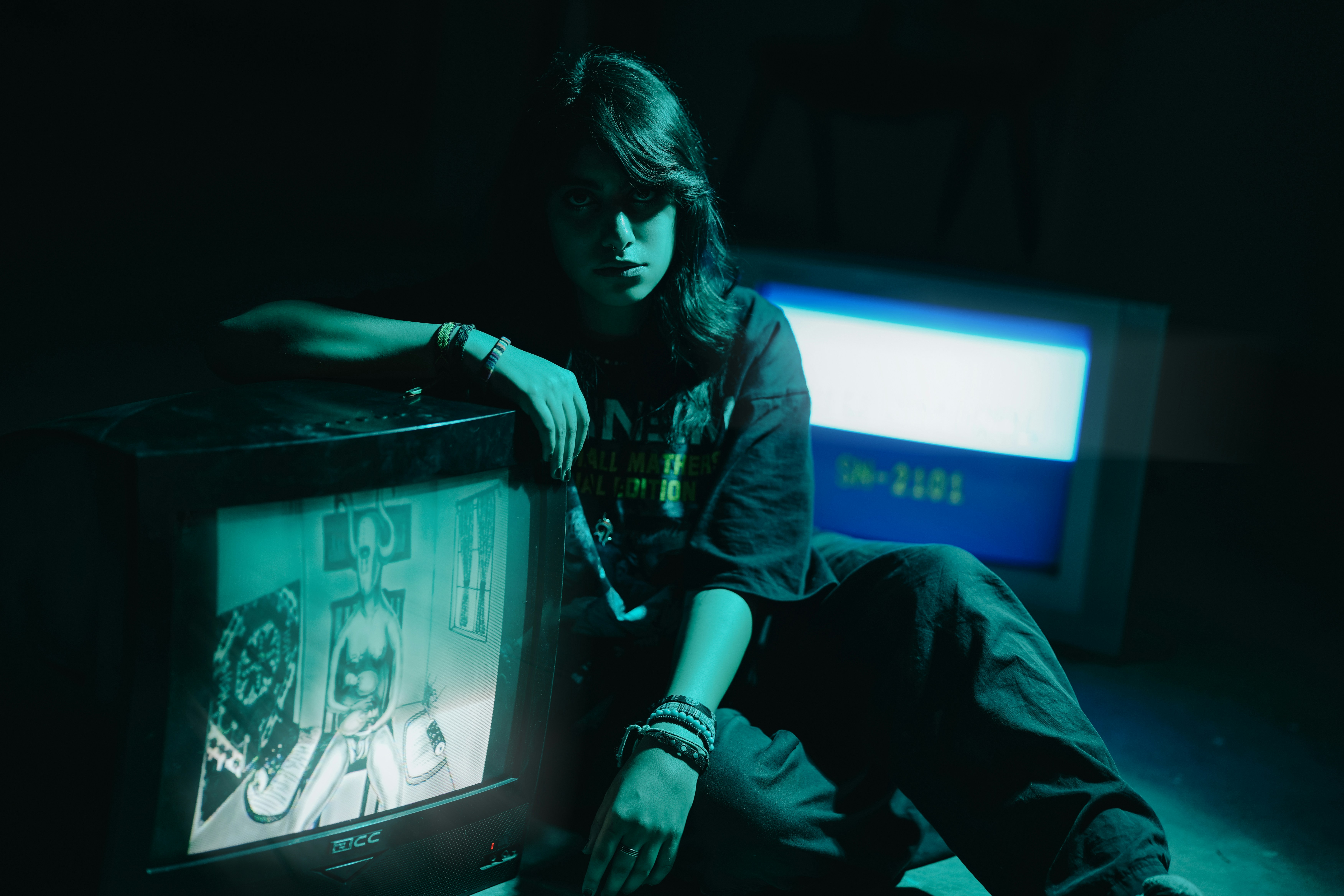 Teenager poses with vintage televisions in blue light