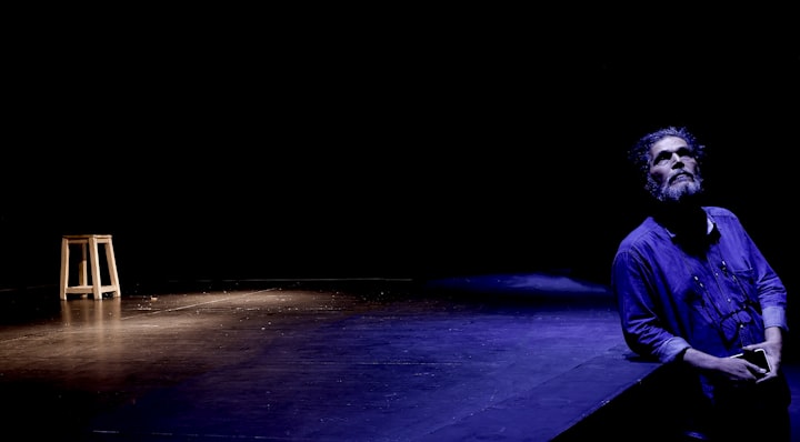 An actor looking upward in a dimly lit theater, face turned away from the camera, dramatic shadows