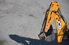 Yellow excavator arm and bucket casting shadow on ground