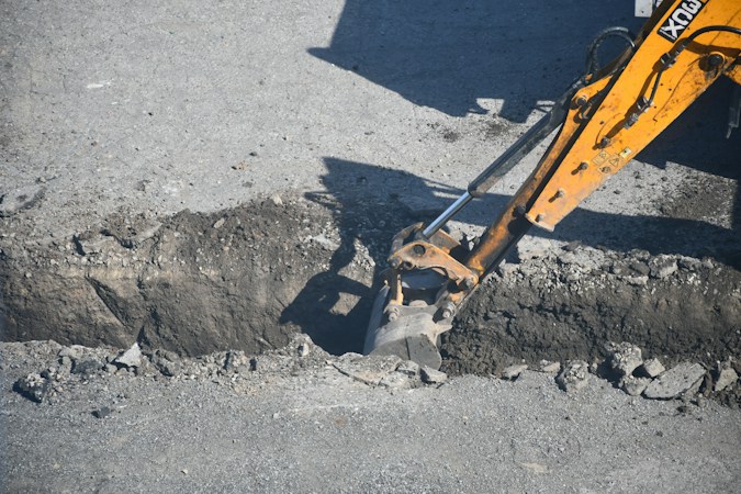 An excavator opening a trench in a paved street to reach a buried utility line