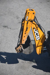 Yellow excavator arm with bucket on asphalt