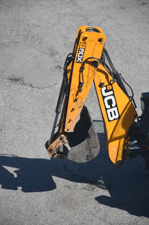 Yellow excavator arm with bucket on asphalt