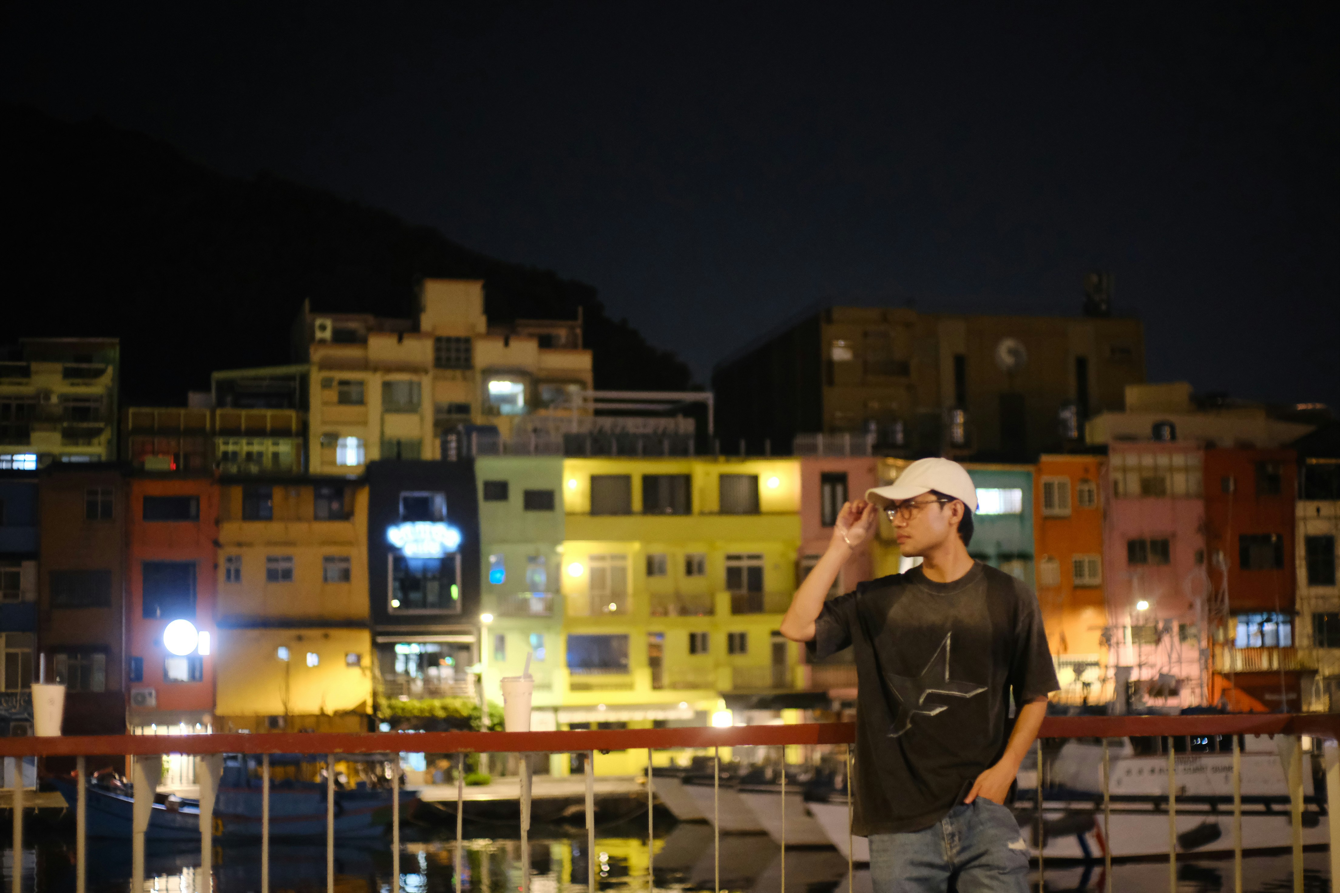Man adjusting glasses with colorful buildings at night.