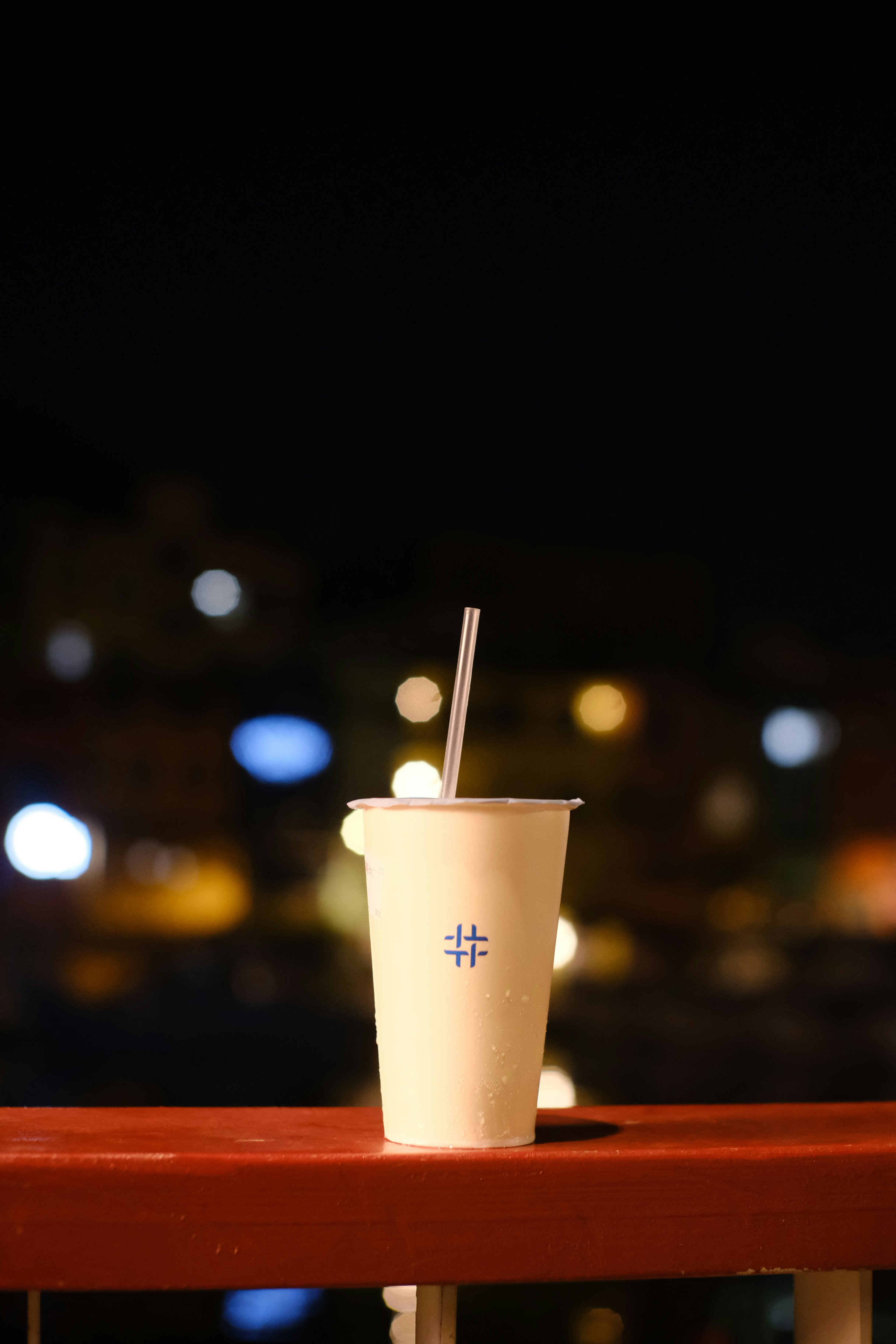 A drink with a straw on a railing at night.