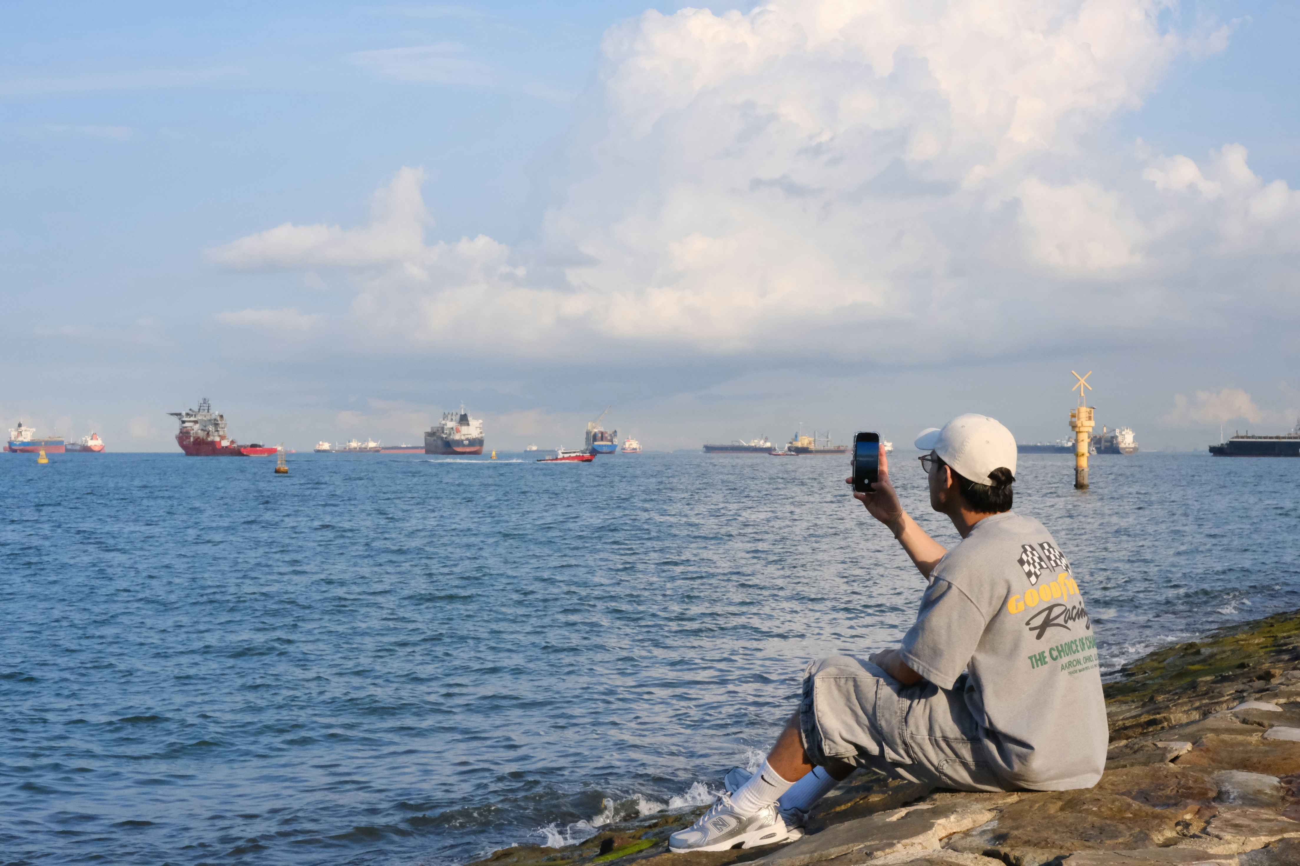 Man with phone by the sea with ships in distance