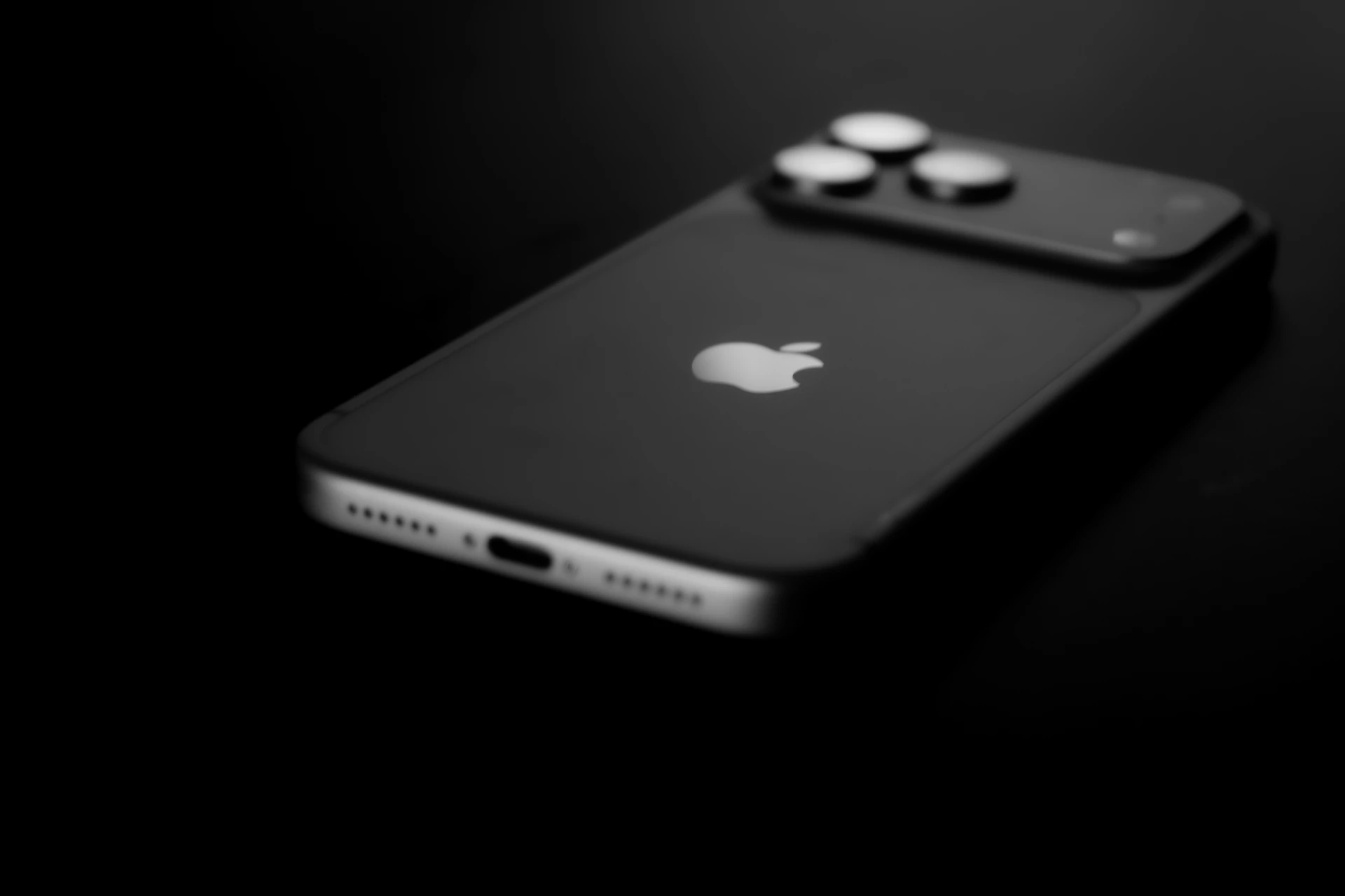 A dark smartphone lies on a black surface.