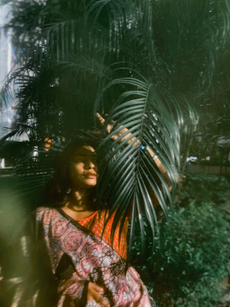 Woman peeking through large palm leaves outdoors.