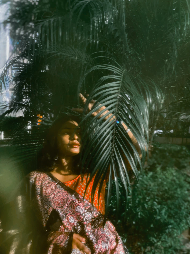 Woman peeking through large palm leaves outdoors.
