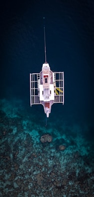 White boat floats over clear blue water and coral reef.