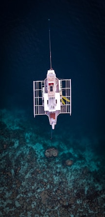 White boat floats over clear blue water and coral reef.