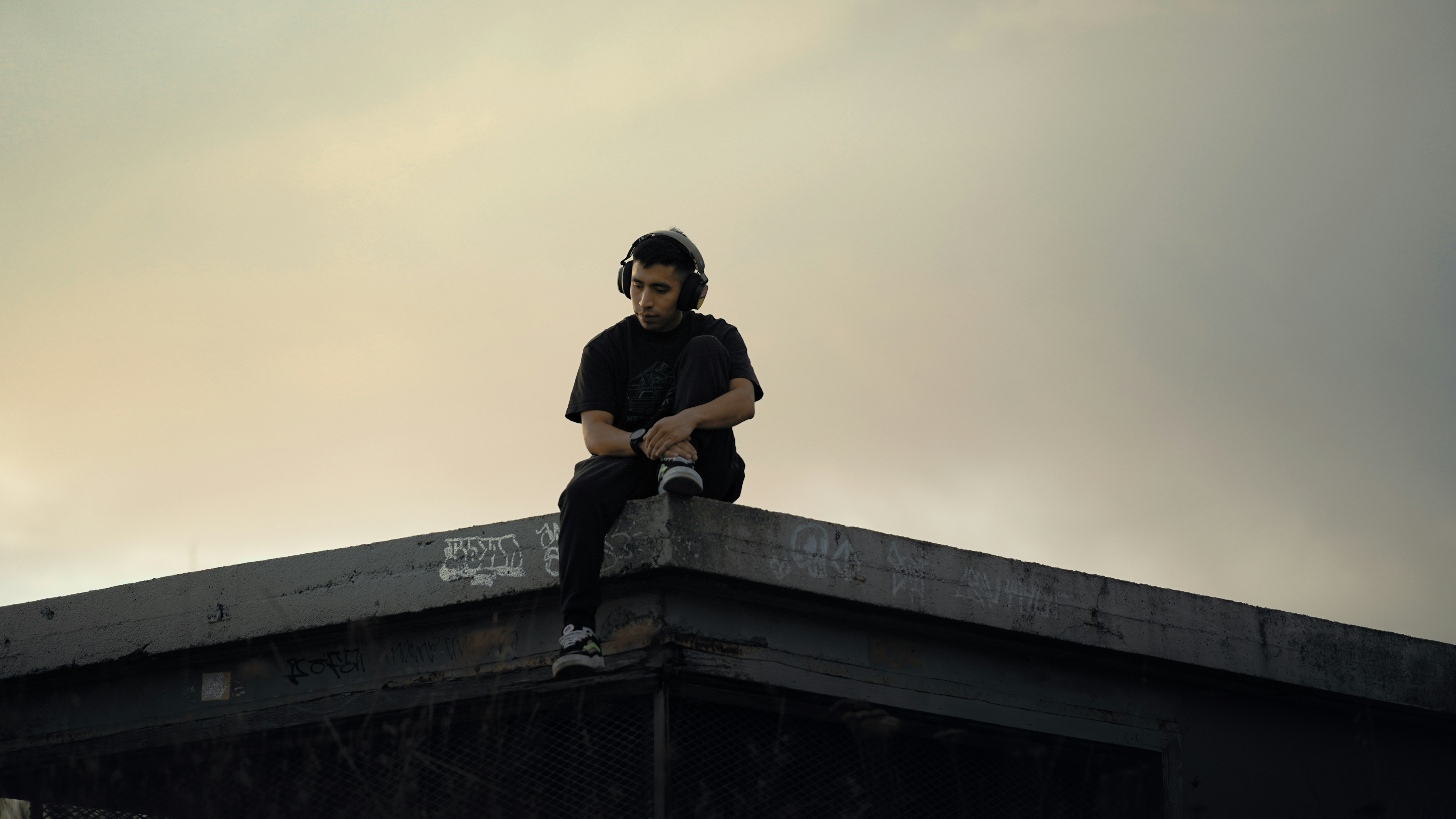 Young person with headphones sitting on rooftop edge.