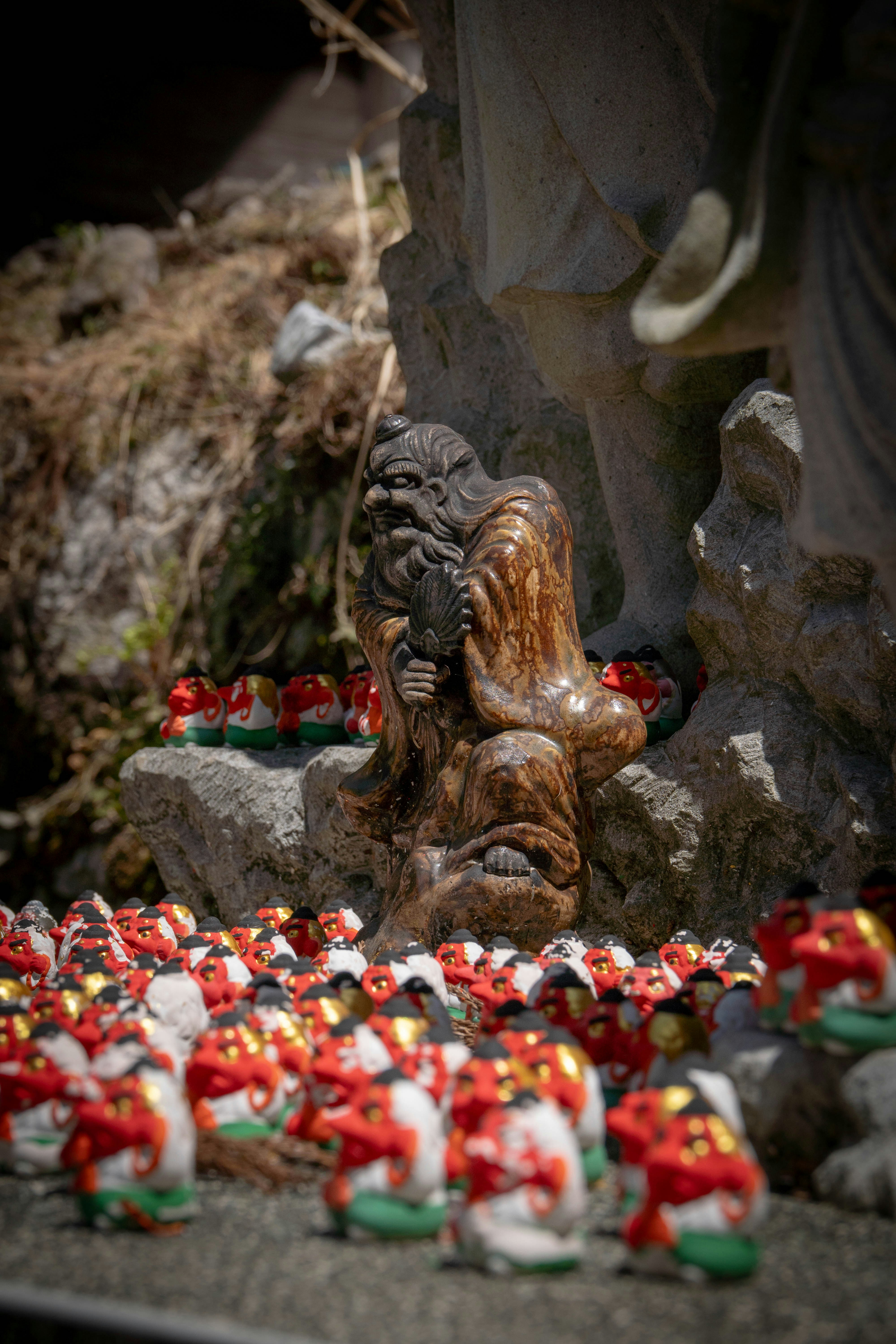 Kleine Tonfiguren mit roten Bändern vor der Statue