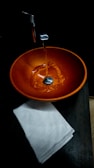 Water flowing into an orange basin with a towel.