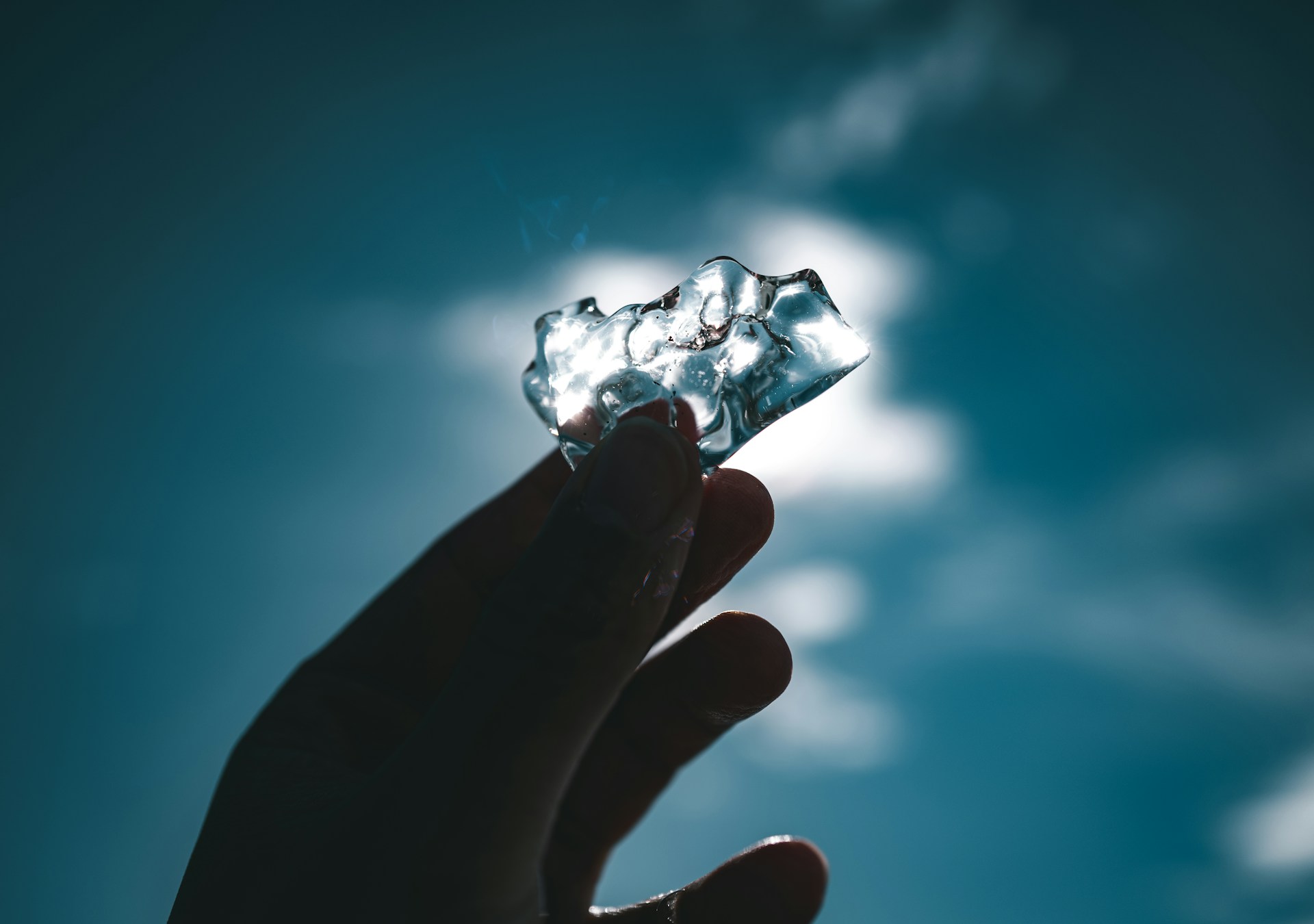 Hand holding a piece of ice against the sky