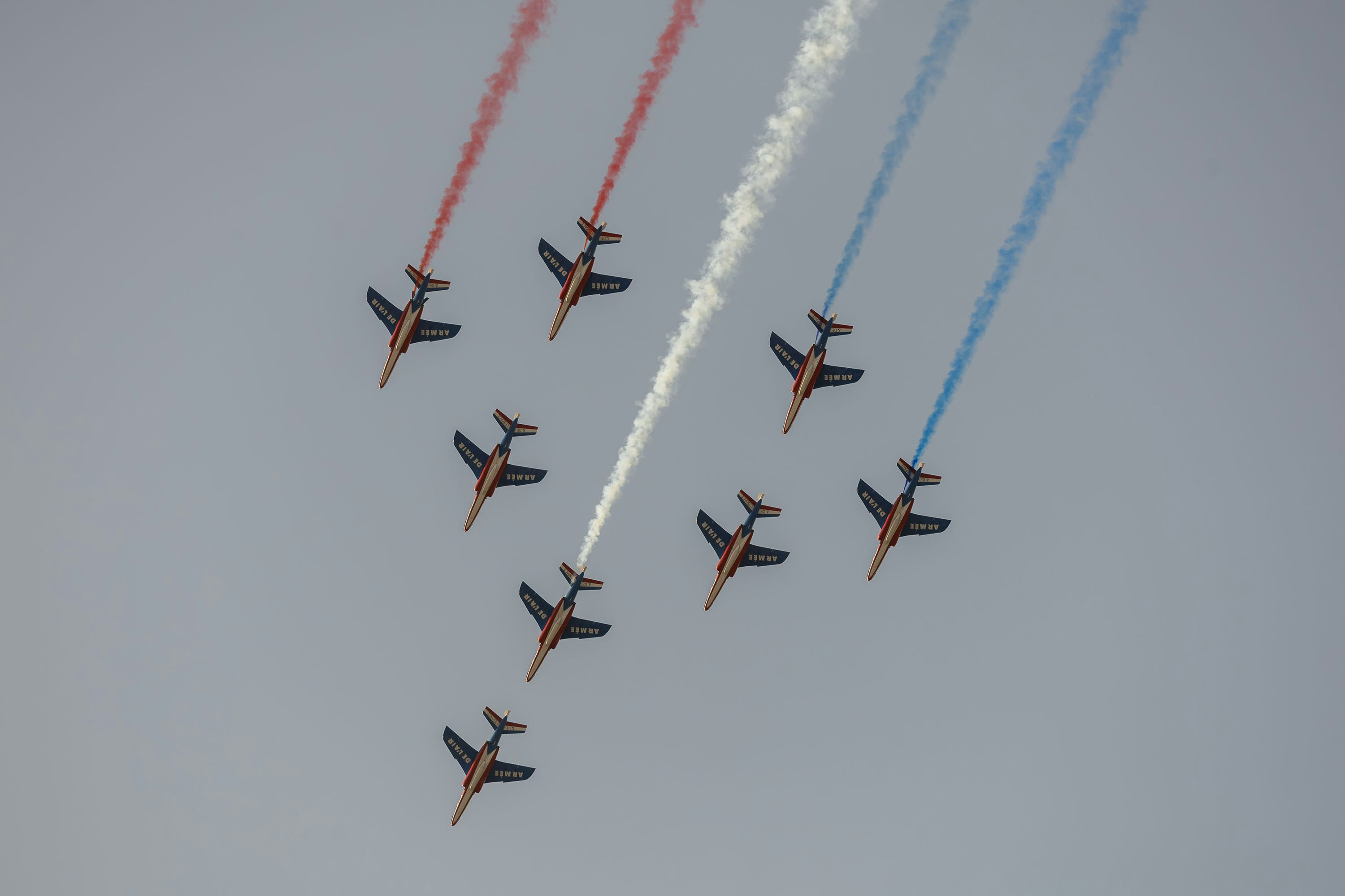 Neun Kampfjets führen eine Flugvorführung mit farbigem Rauch vor.