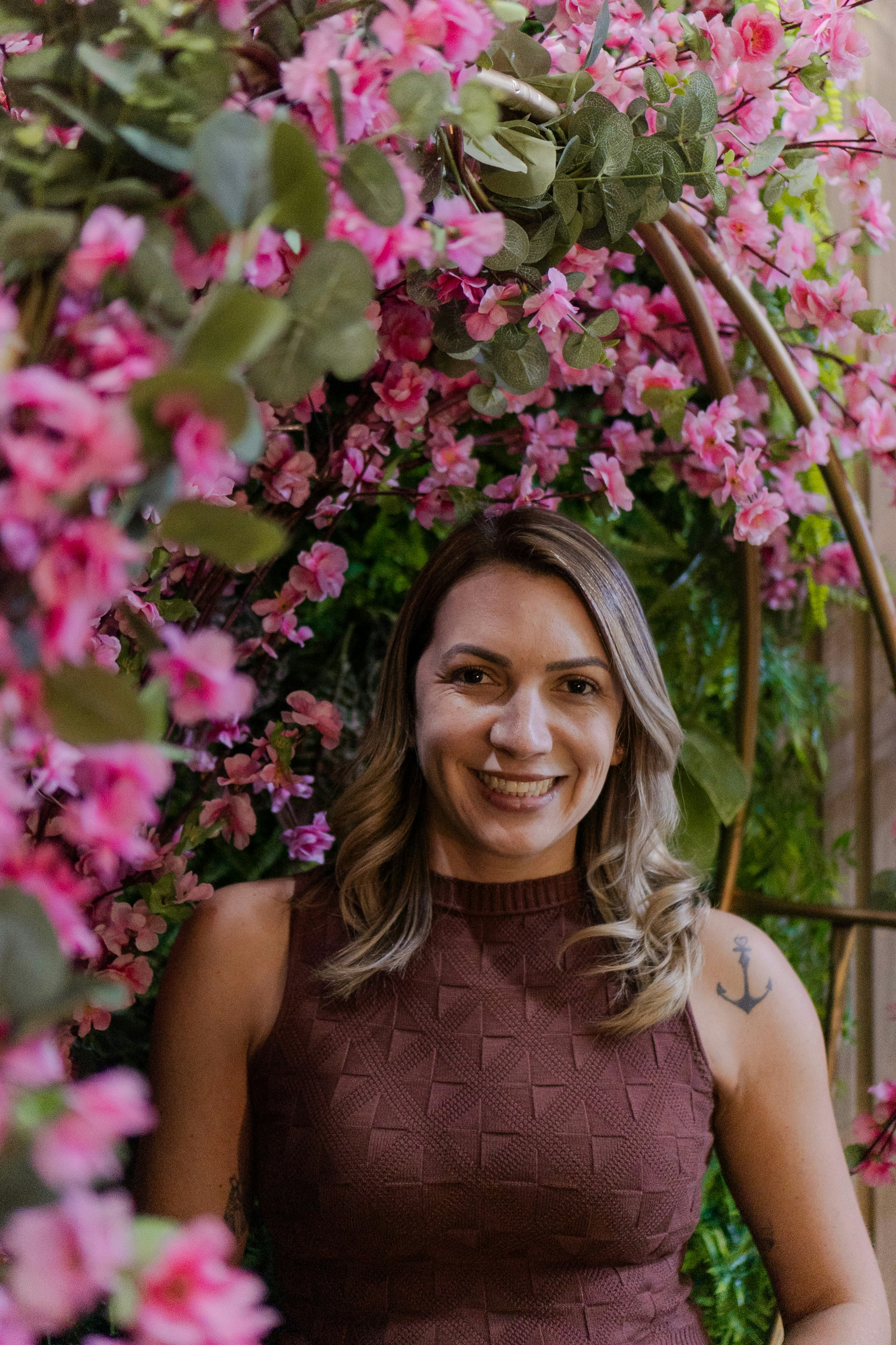 Woman smiling amidst pink flowers and greenery.