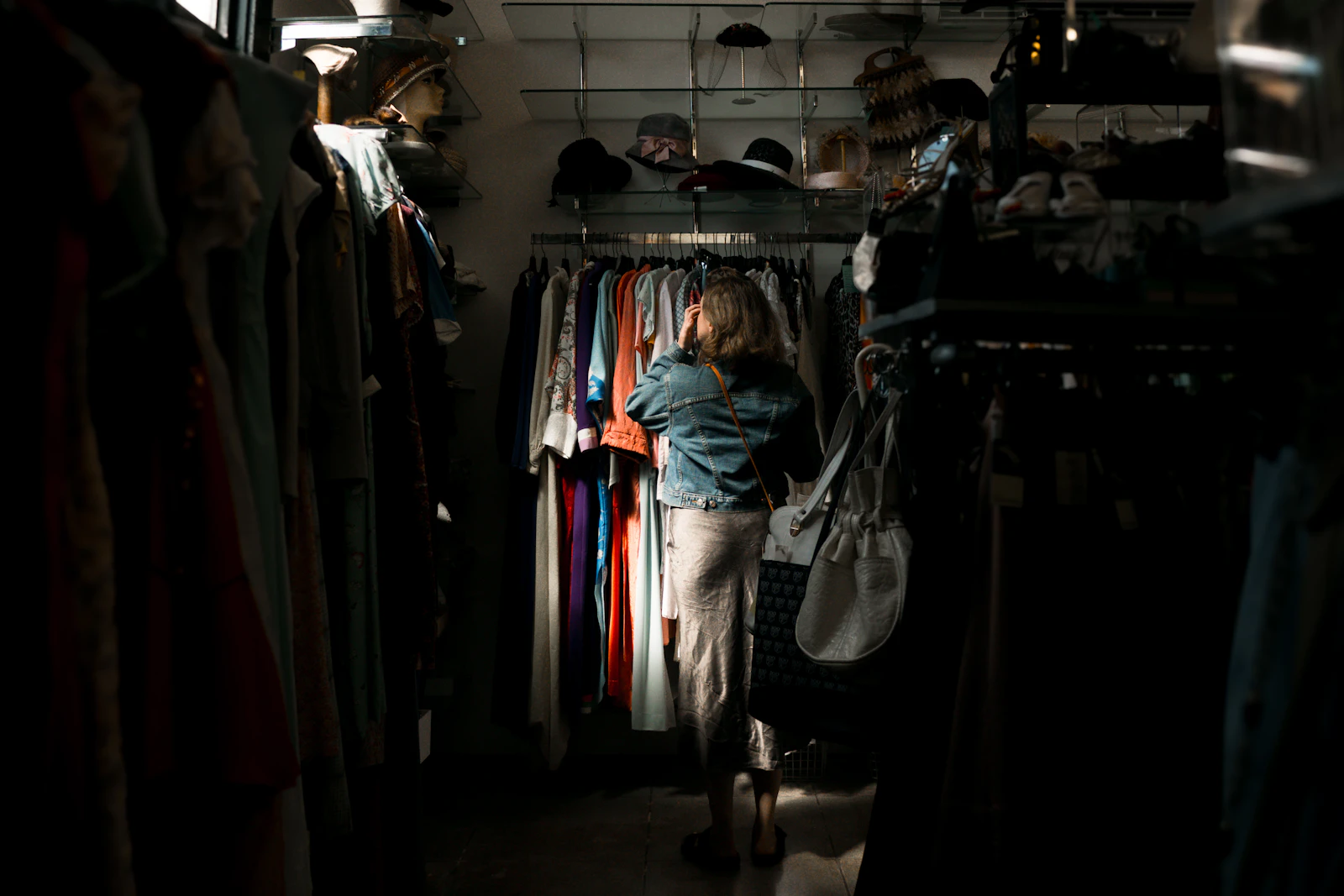 A woman browsing clothing on a rack in a moody, purple-lit retail store.