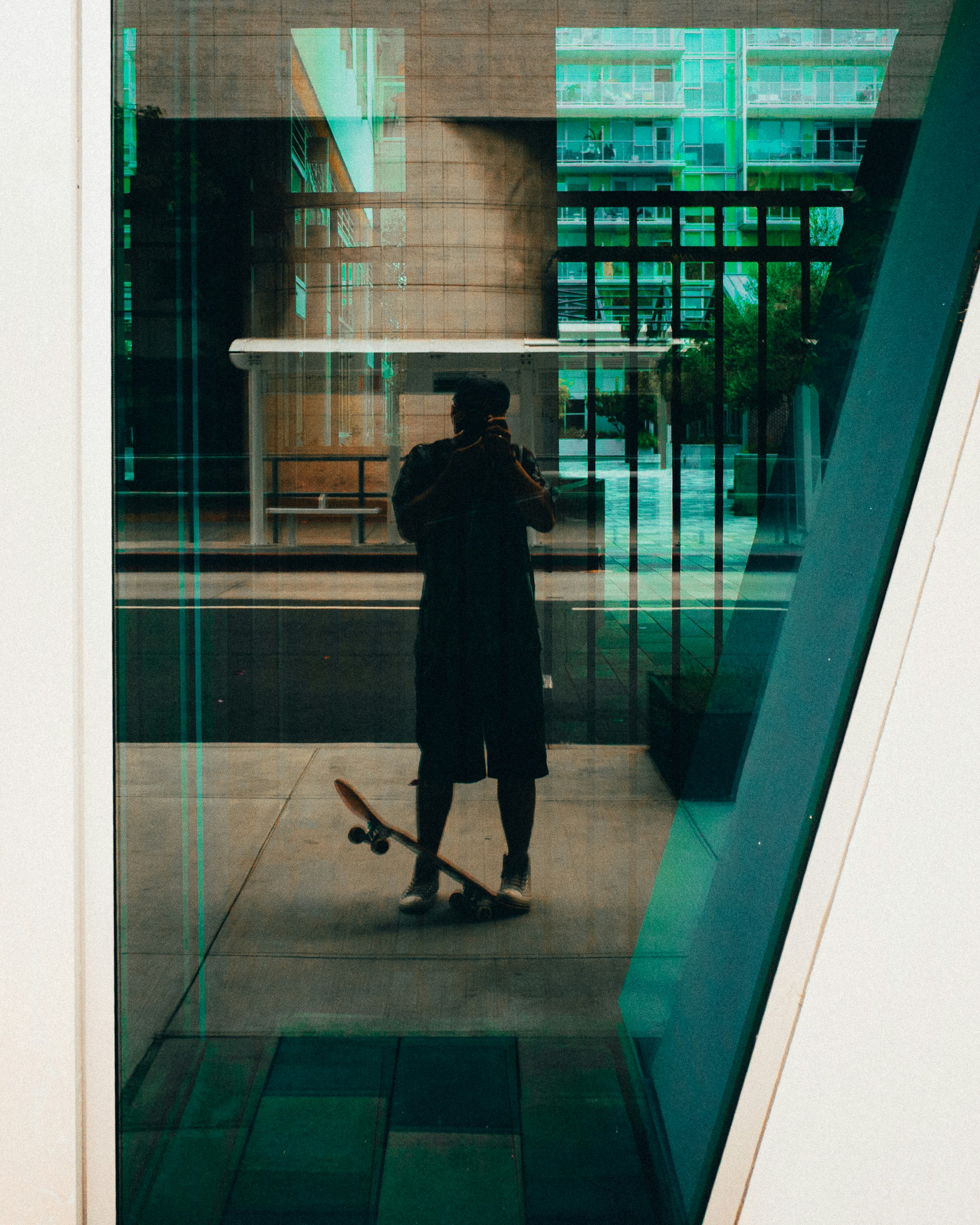 Man with skateboard takes reflection selfie outside building