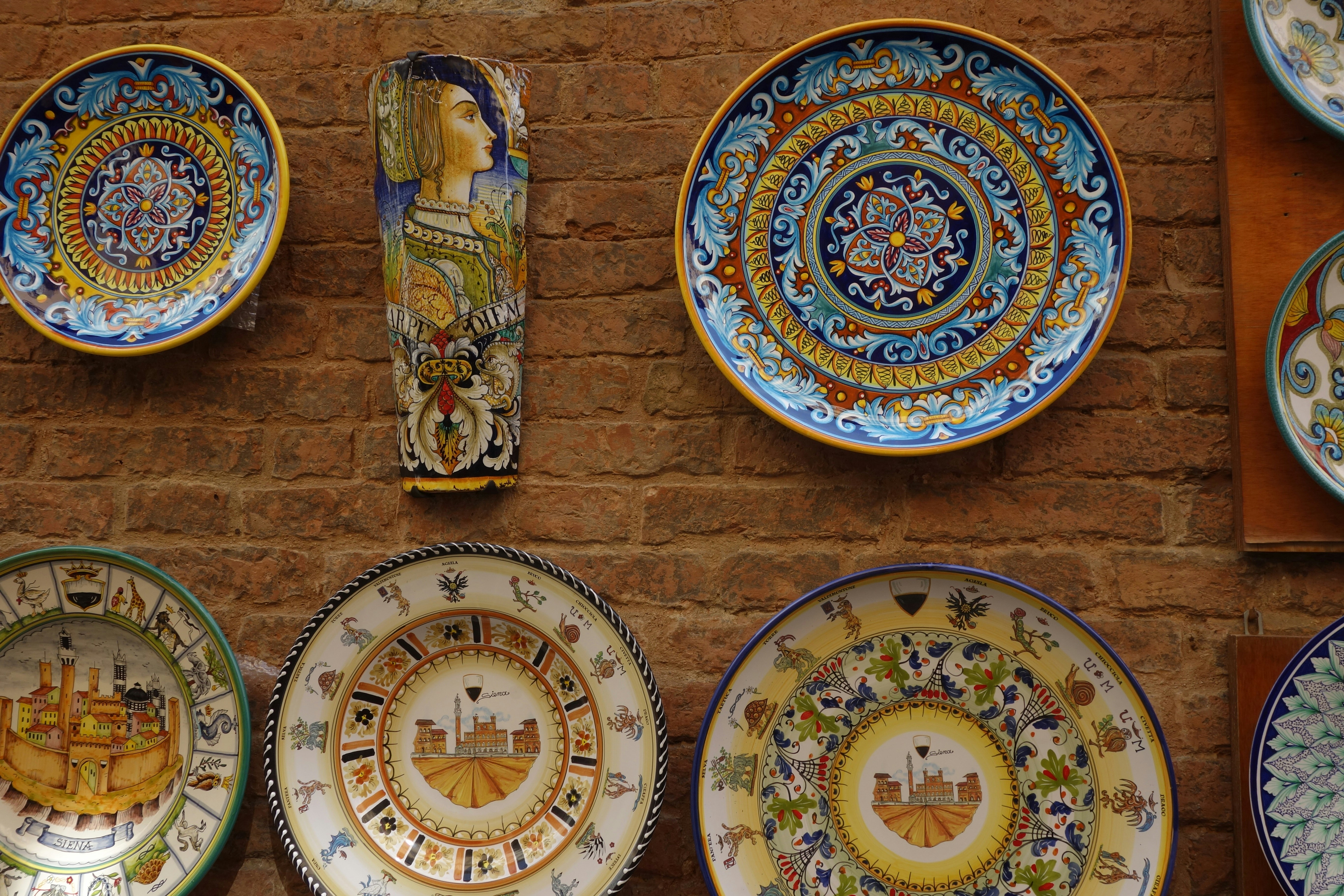 Ornate ceramic plates and vase displayed on brick wall.